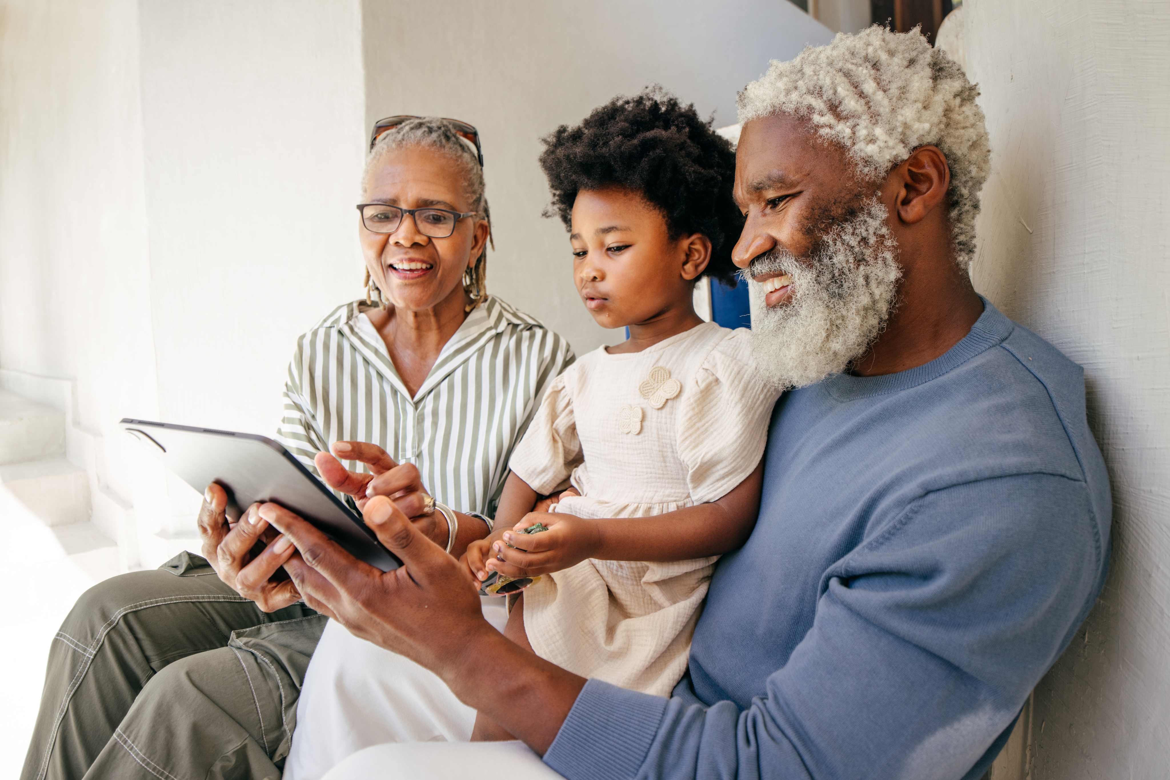 African American grandparents and grandchild looking at tablet together smiling