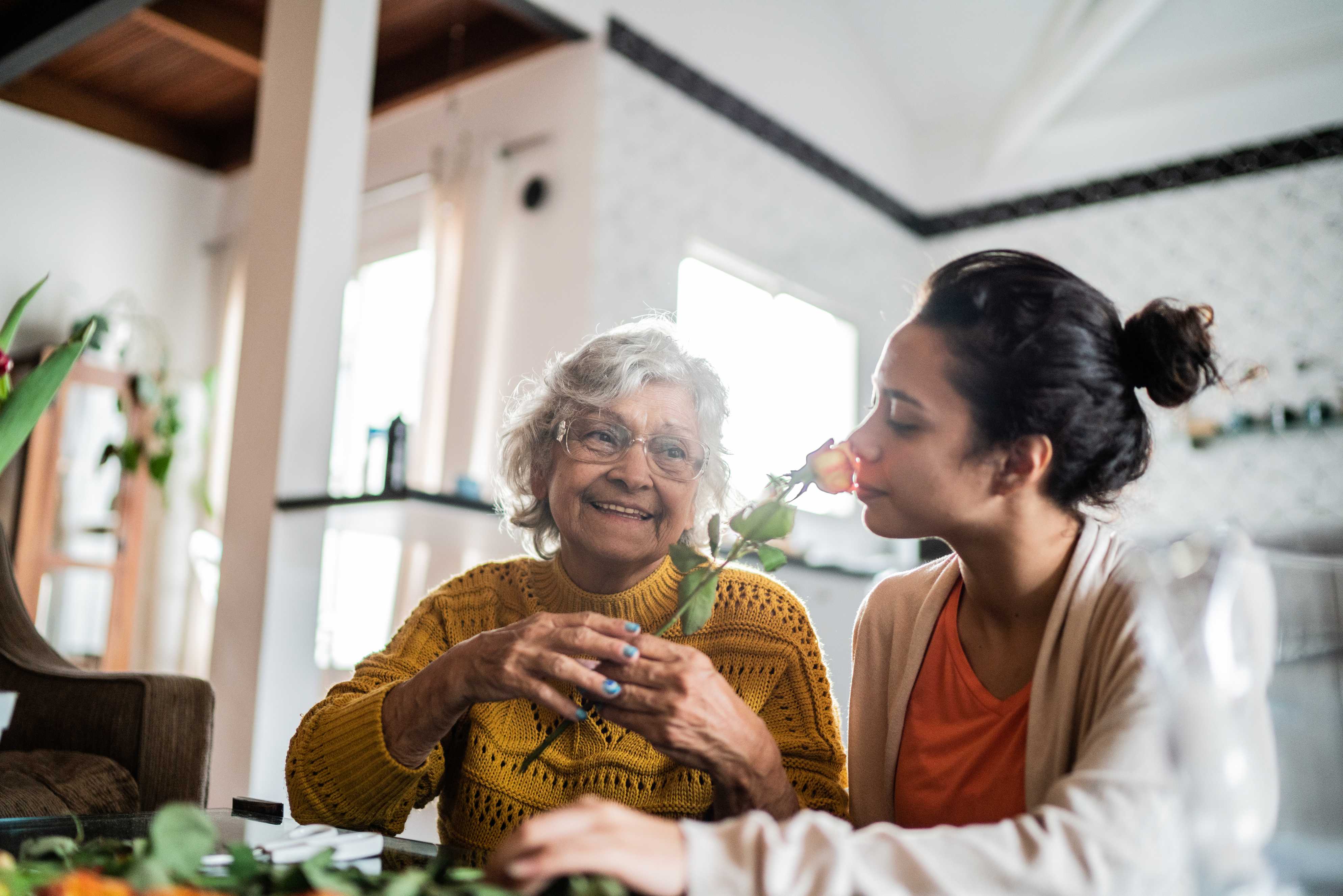 Elderly woman and younger woman sharing moment with rose in kitchen
