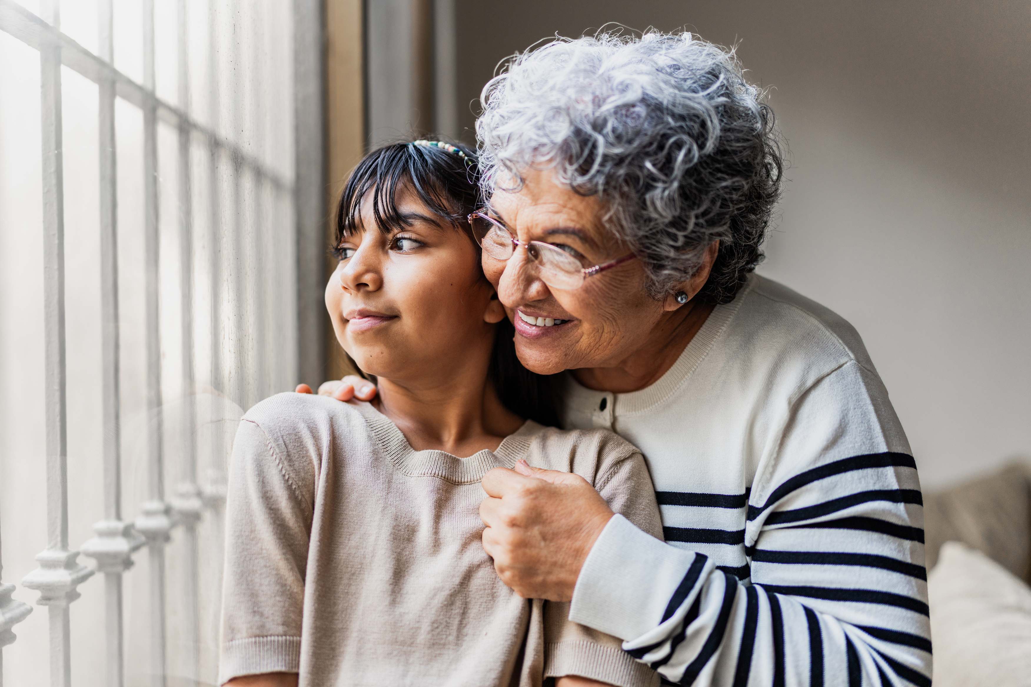 Elderly woman with gray hair embracing younger woman by window