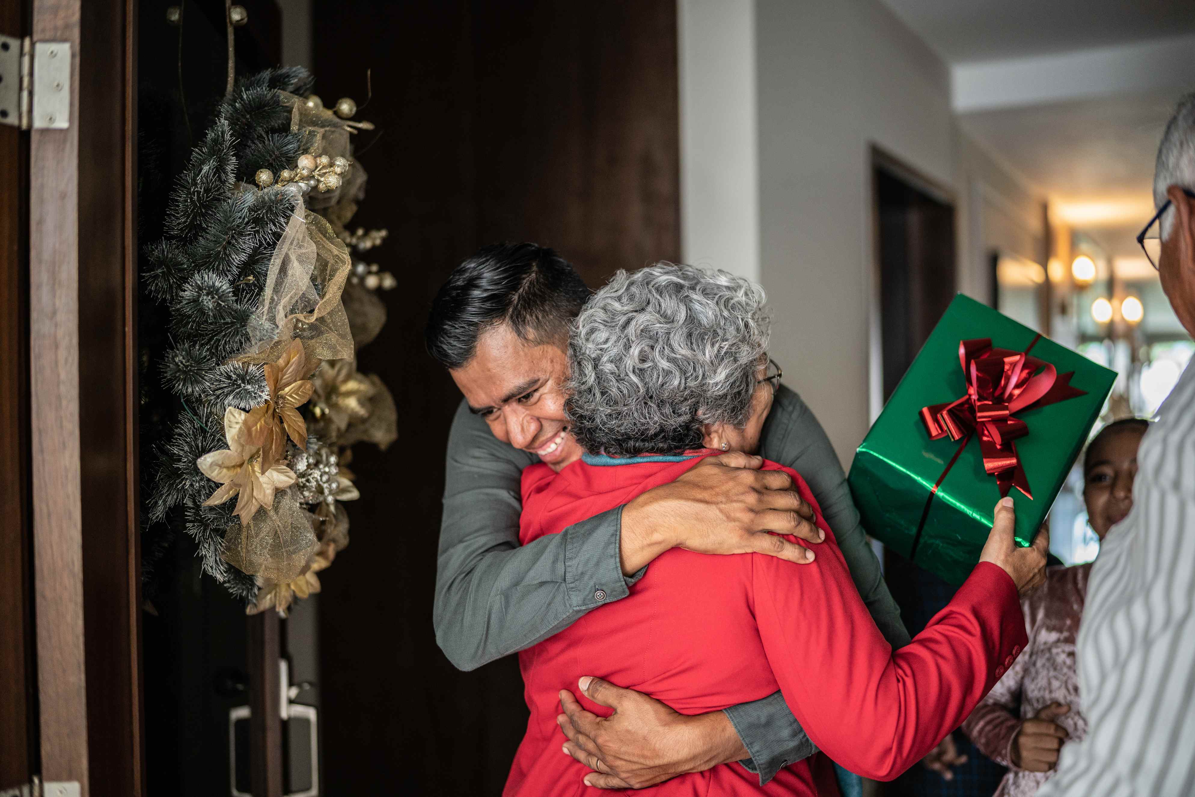 Family embracing at doorway during holiday visit with wrapped gift