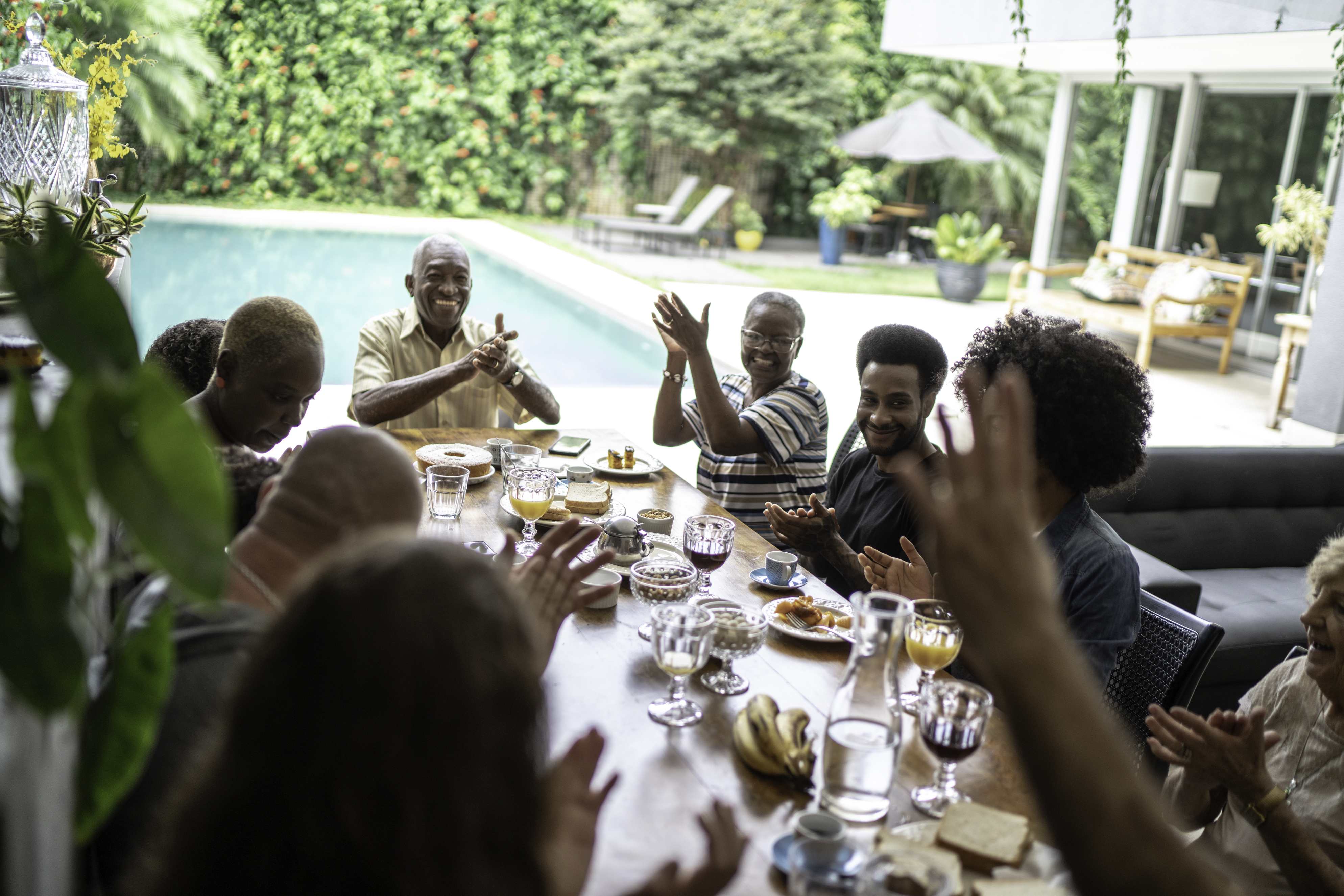 Family gathering around dining table by pool celebrating together