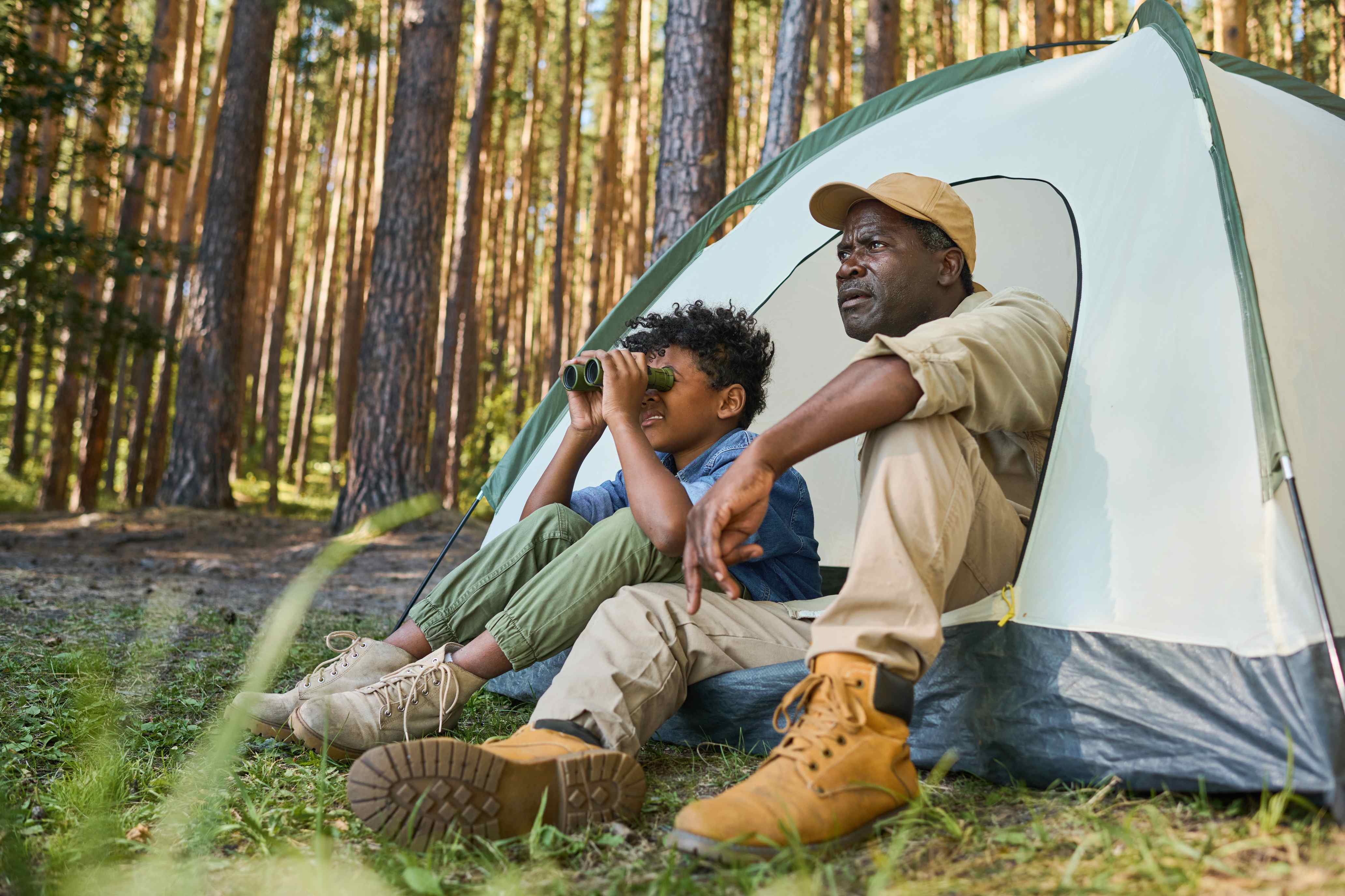 Father and son camping in forest using binoculars from tent