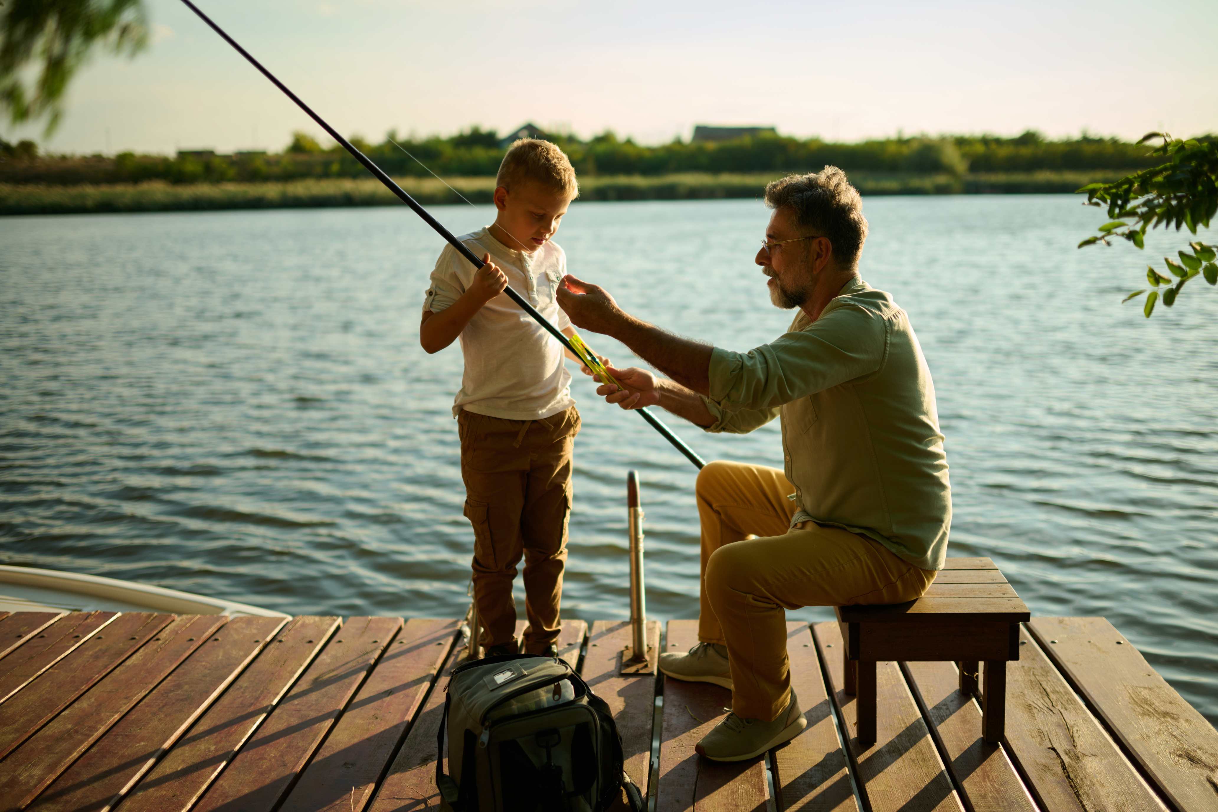 Father teaching young son to fish on wooden dock at sunset