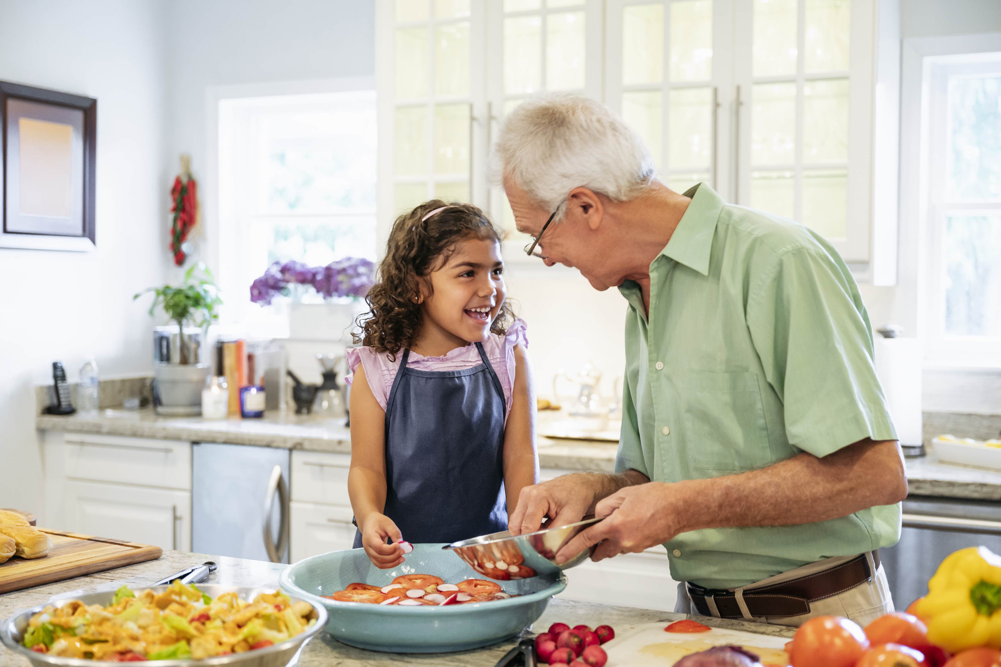 Grandfather and granddaughter cooking together in bright kitchen