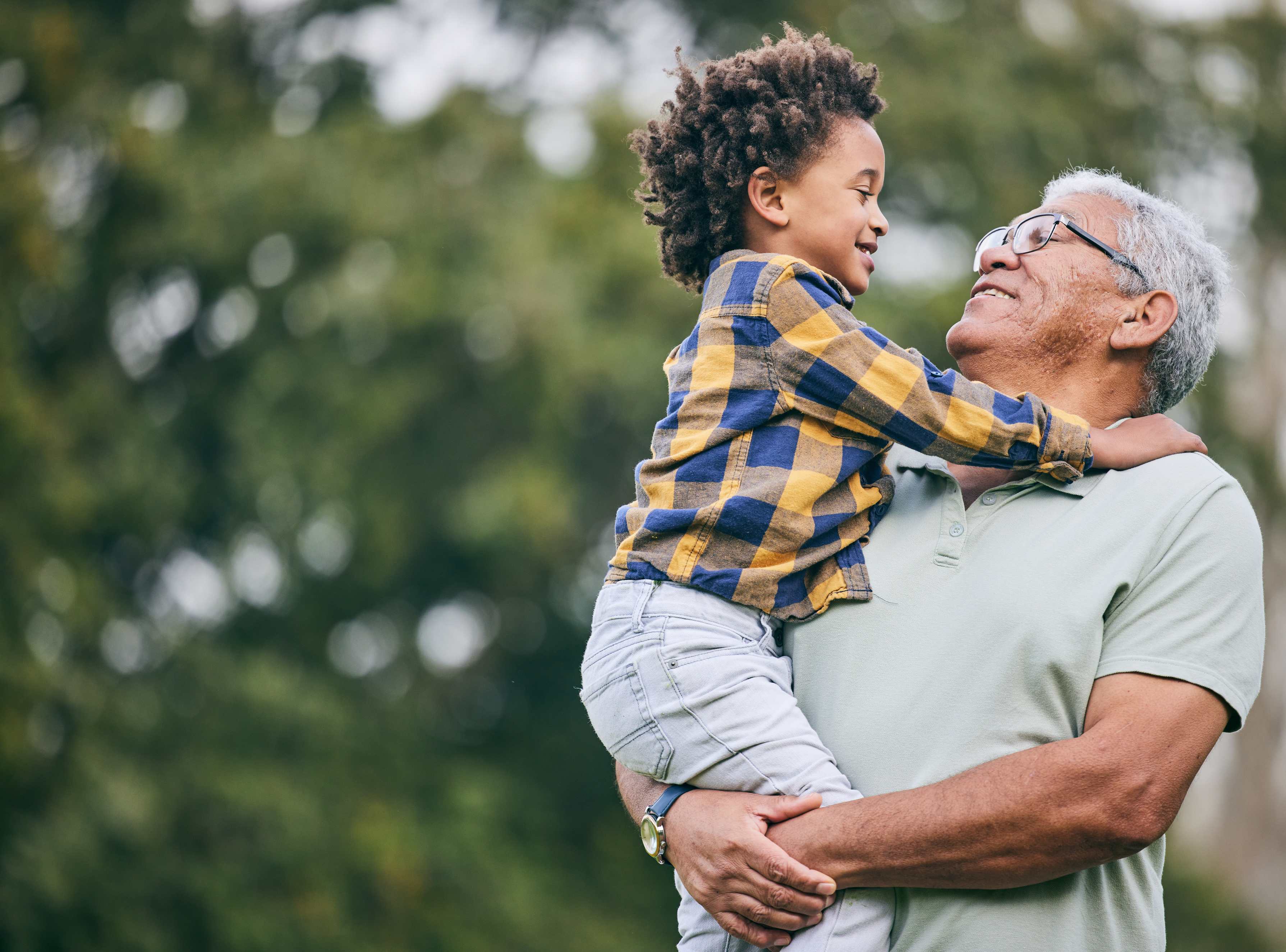 Grandfather holding young grandson outdoors, both smiling at each other