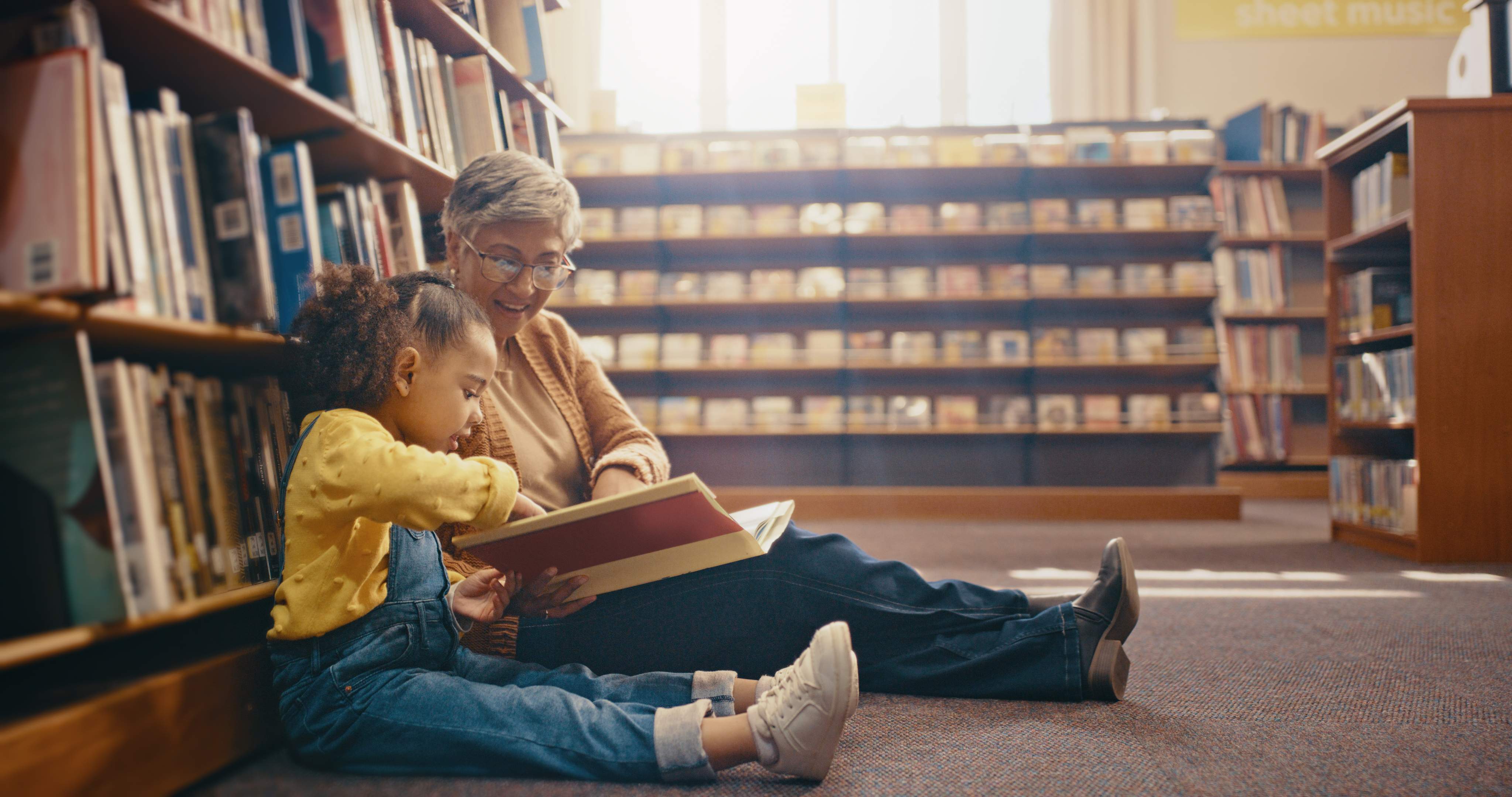 Grandmother and child reading book together on library floor