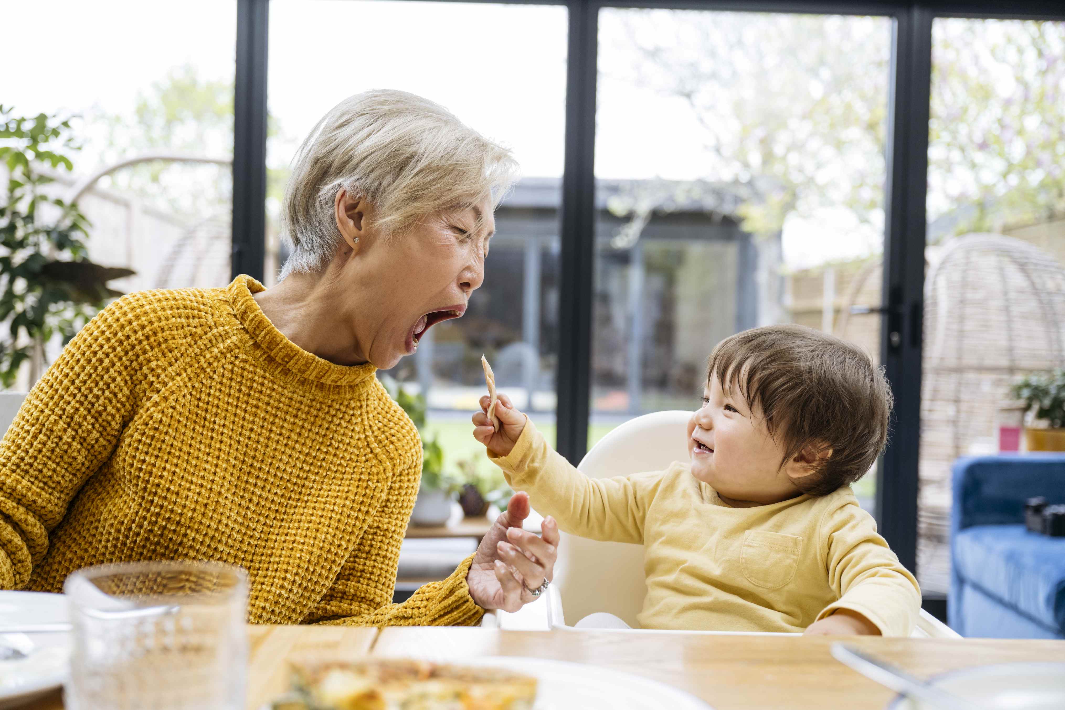 Grandmother and toddler sharing food together in bright kitchen