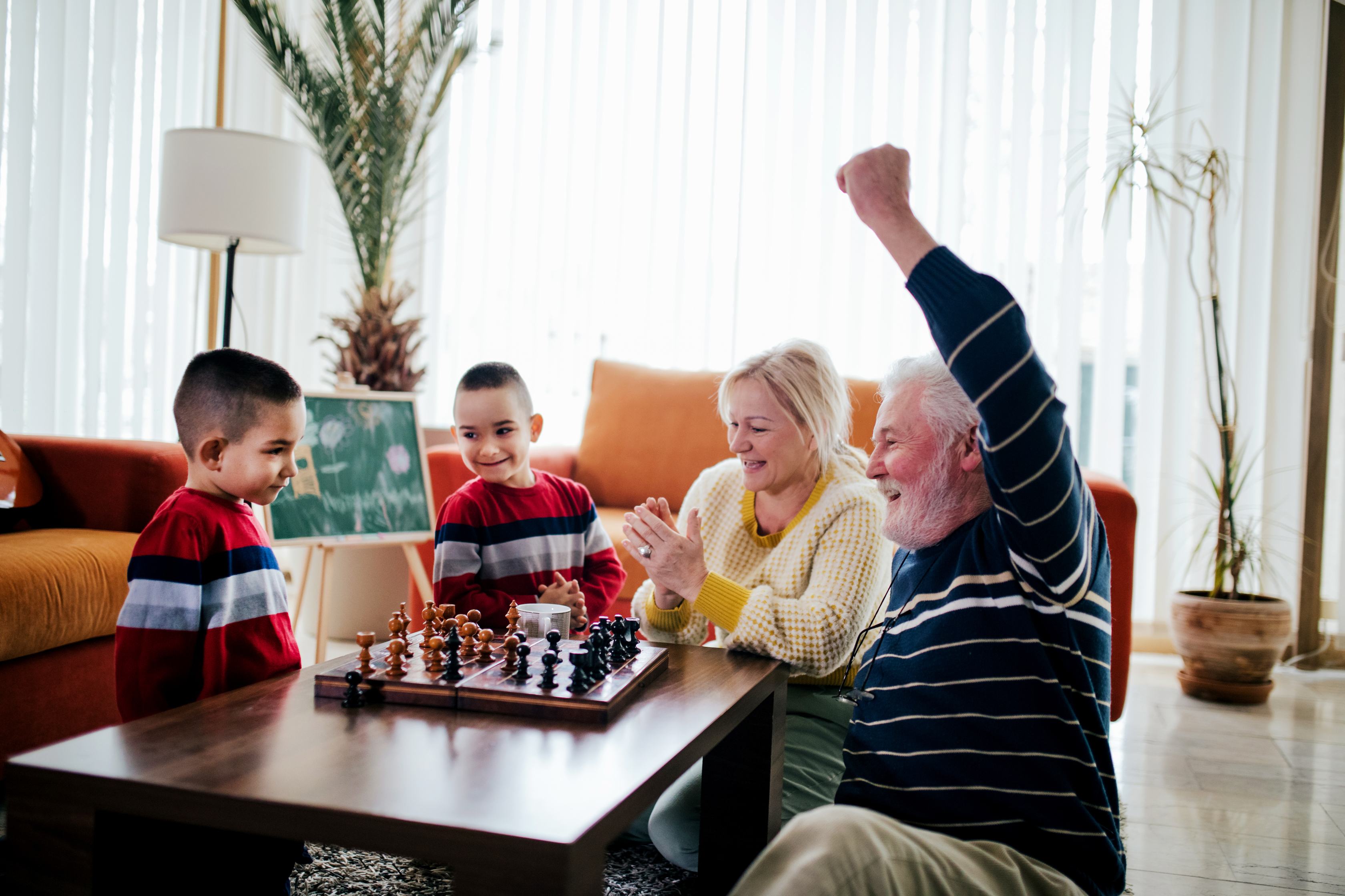 Grandparents celebrating chess victory with two young boys in living room