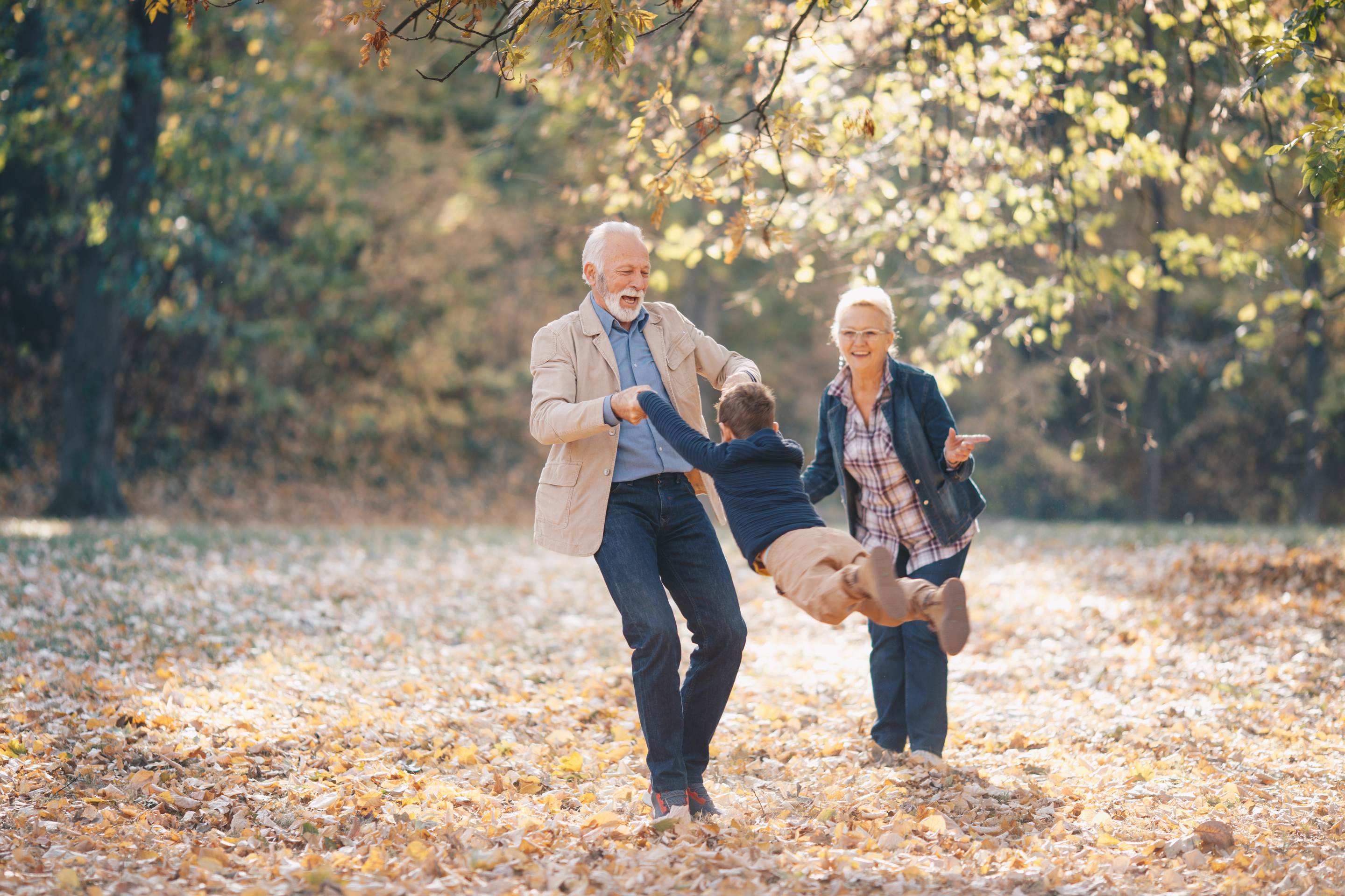 Grandparents playing with child in autumn park with fallen leaves