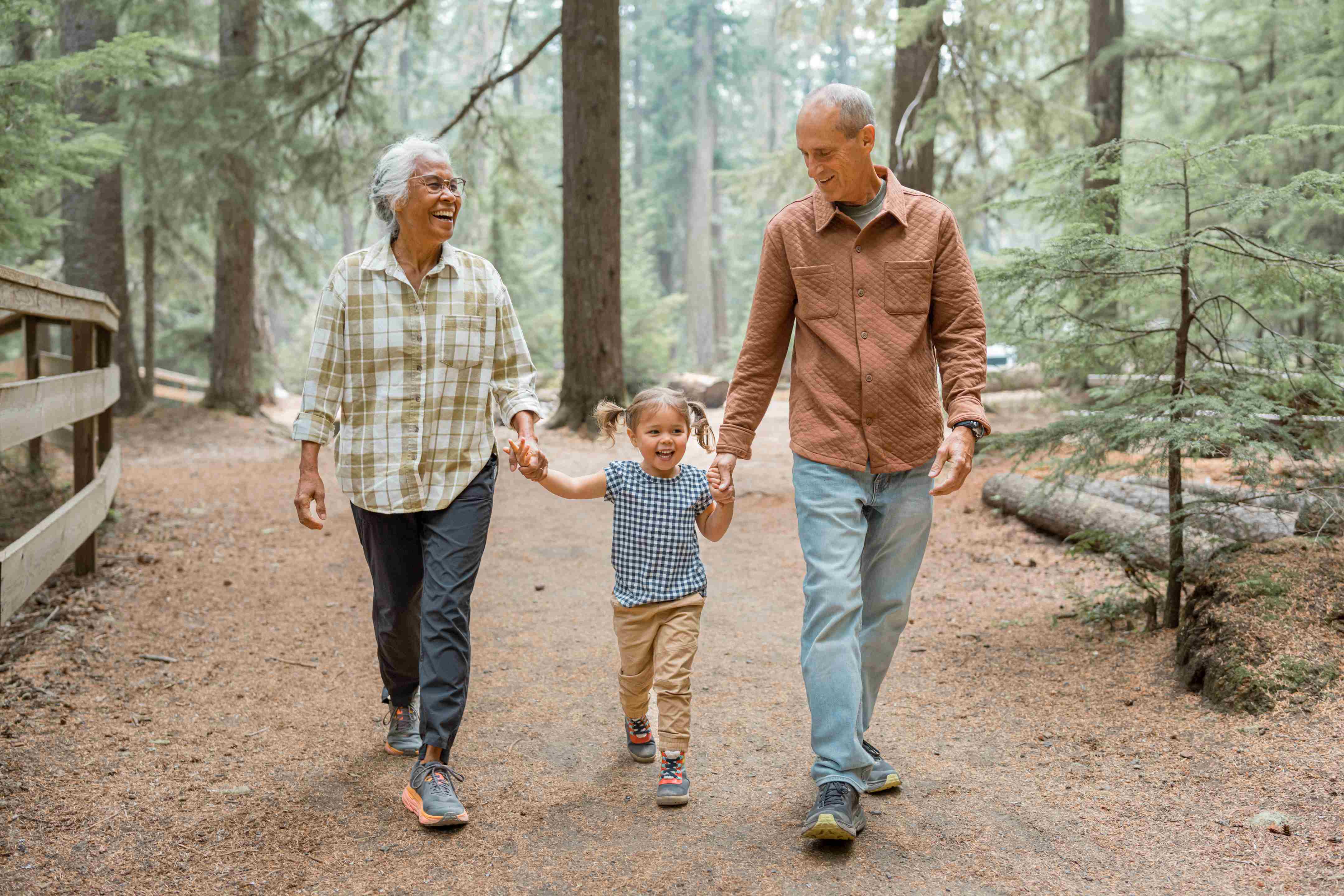 Grandparents walking with young grandchild on forest trail holding hands