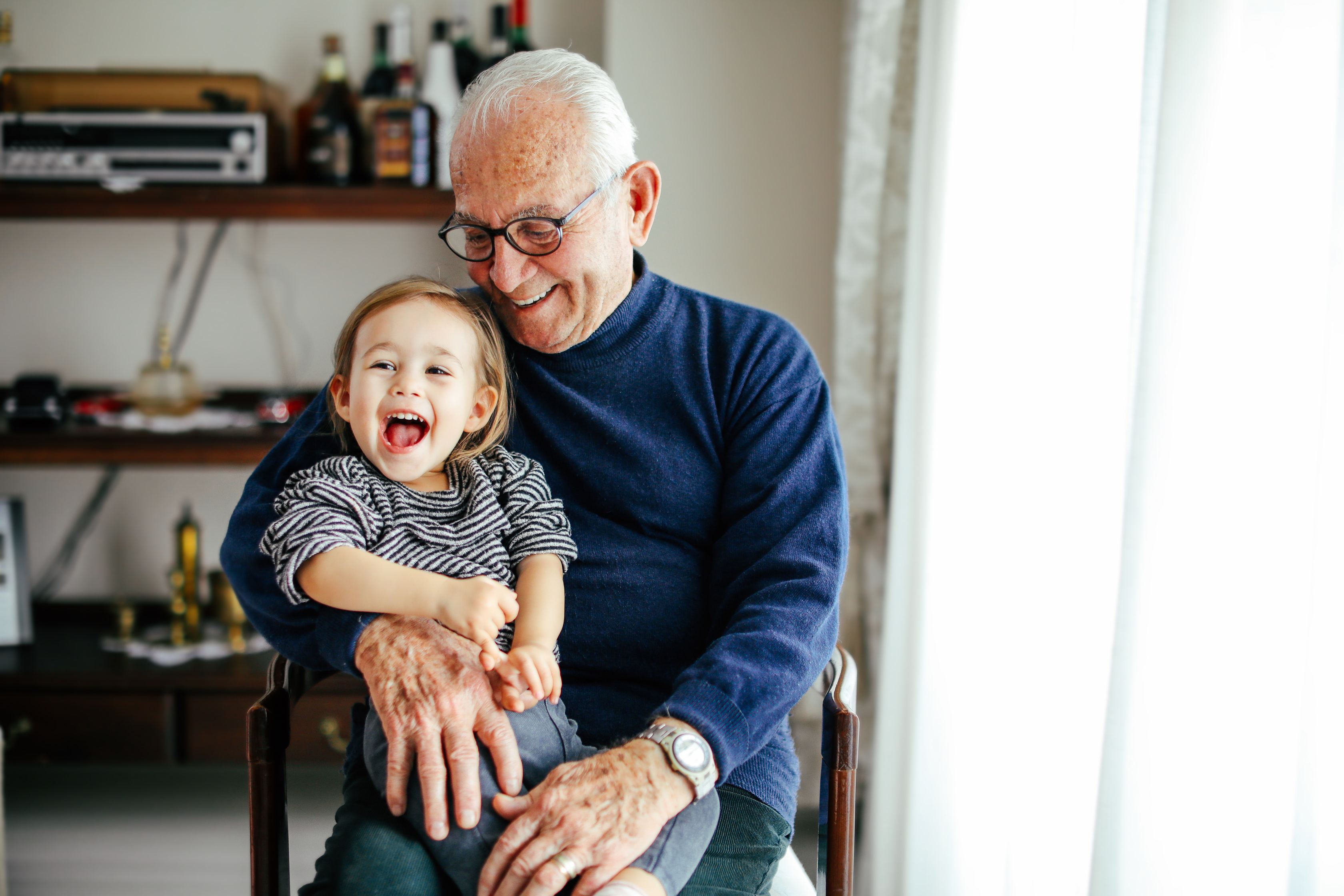 Happy elderly grandfather hugging laughing young grandchild in home