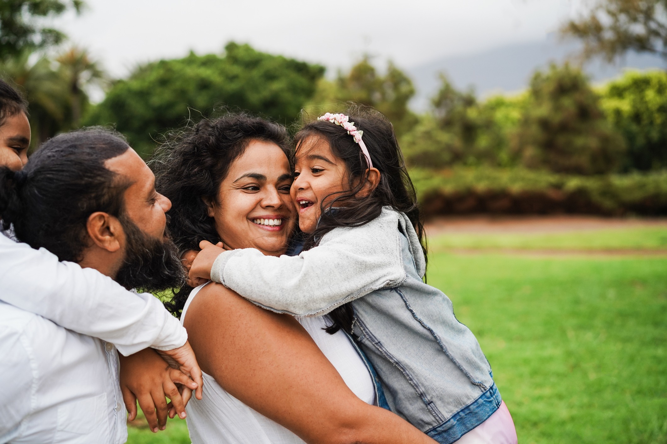 Happy family embracing outdoors in park with green trees