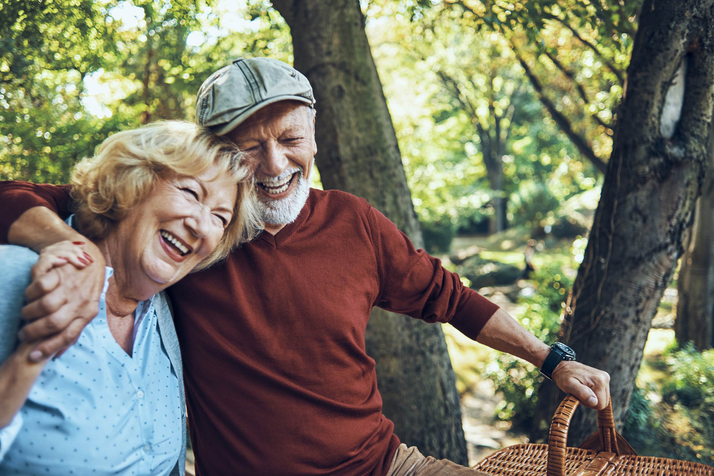 Happy senior couple laughing together in sunny park with picnic basket