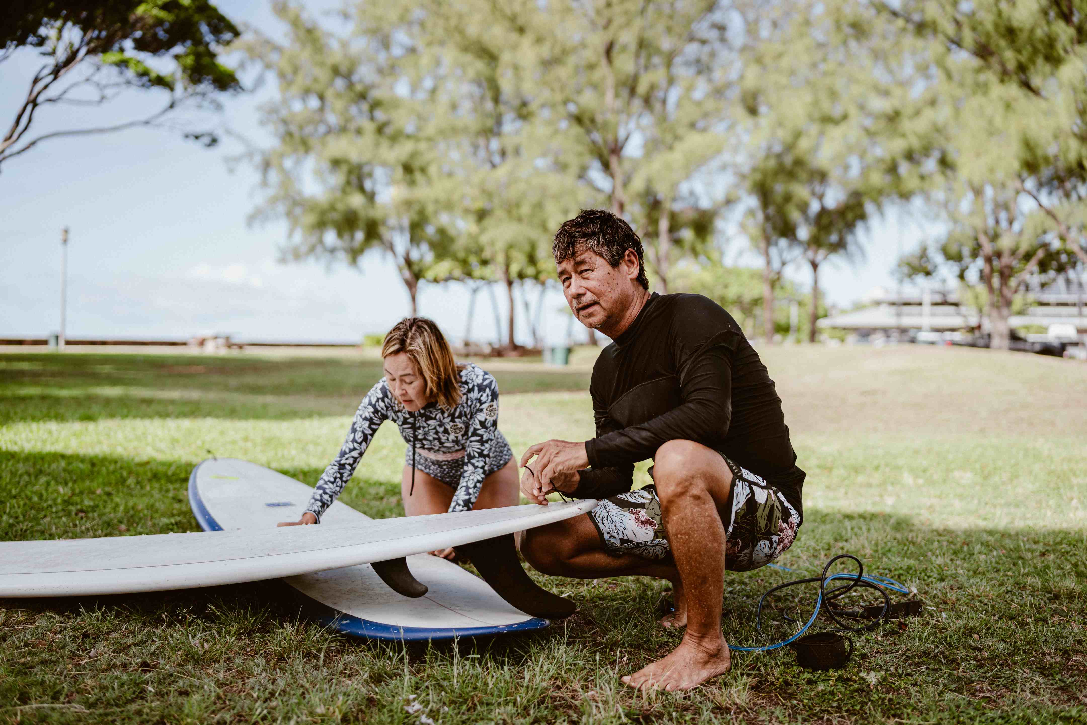 Man and woman preparing surfboards on grass near beach