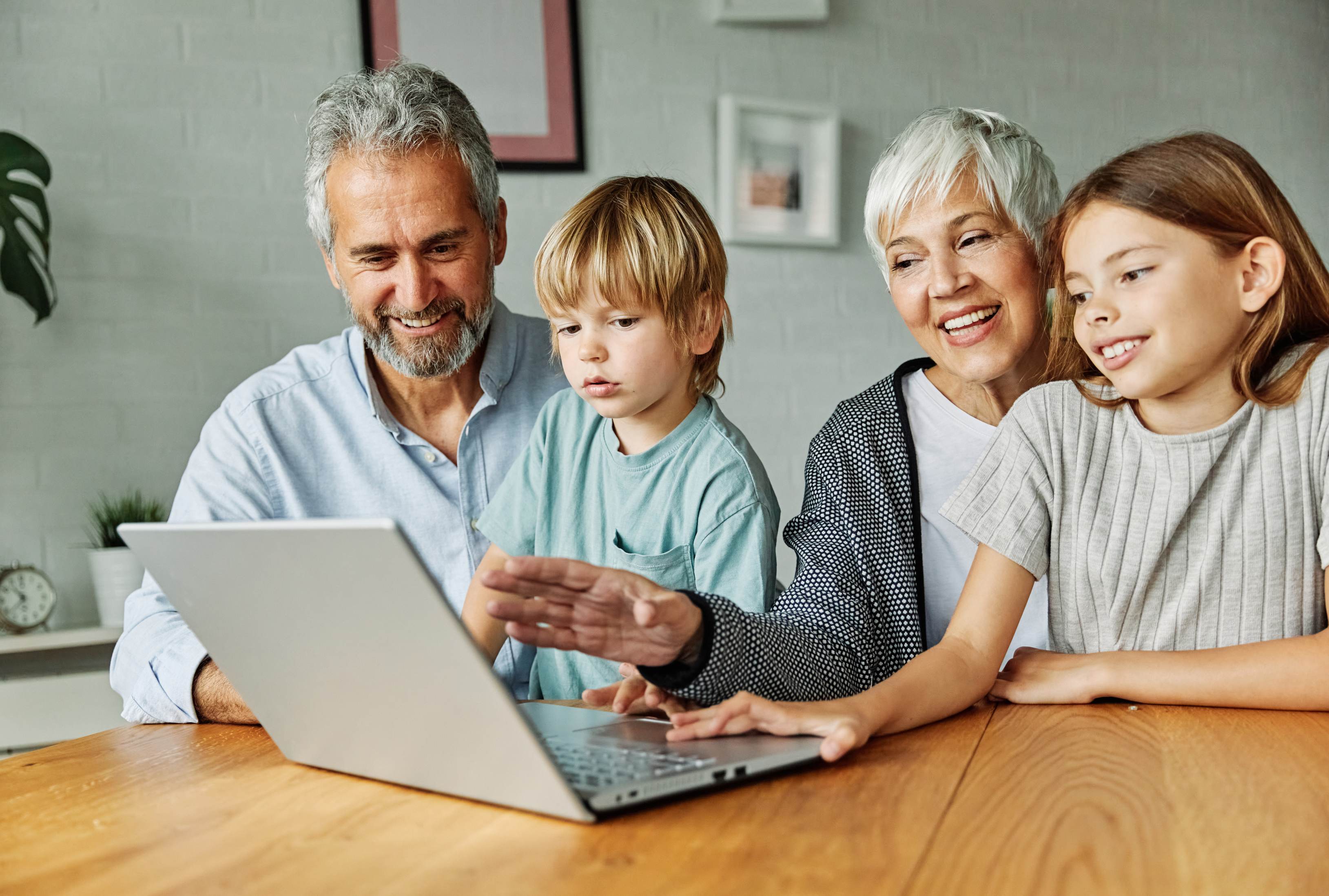 Multi-generational family of four including grandparents and two children gathered around laptop computer at wooden table