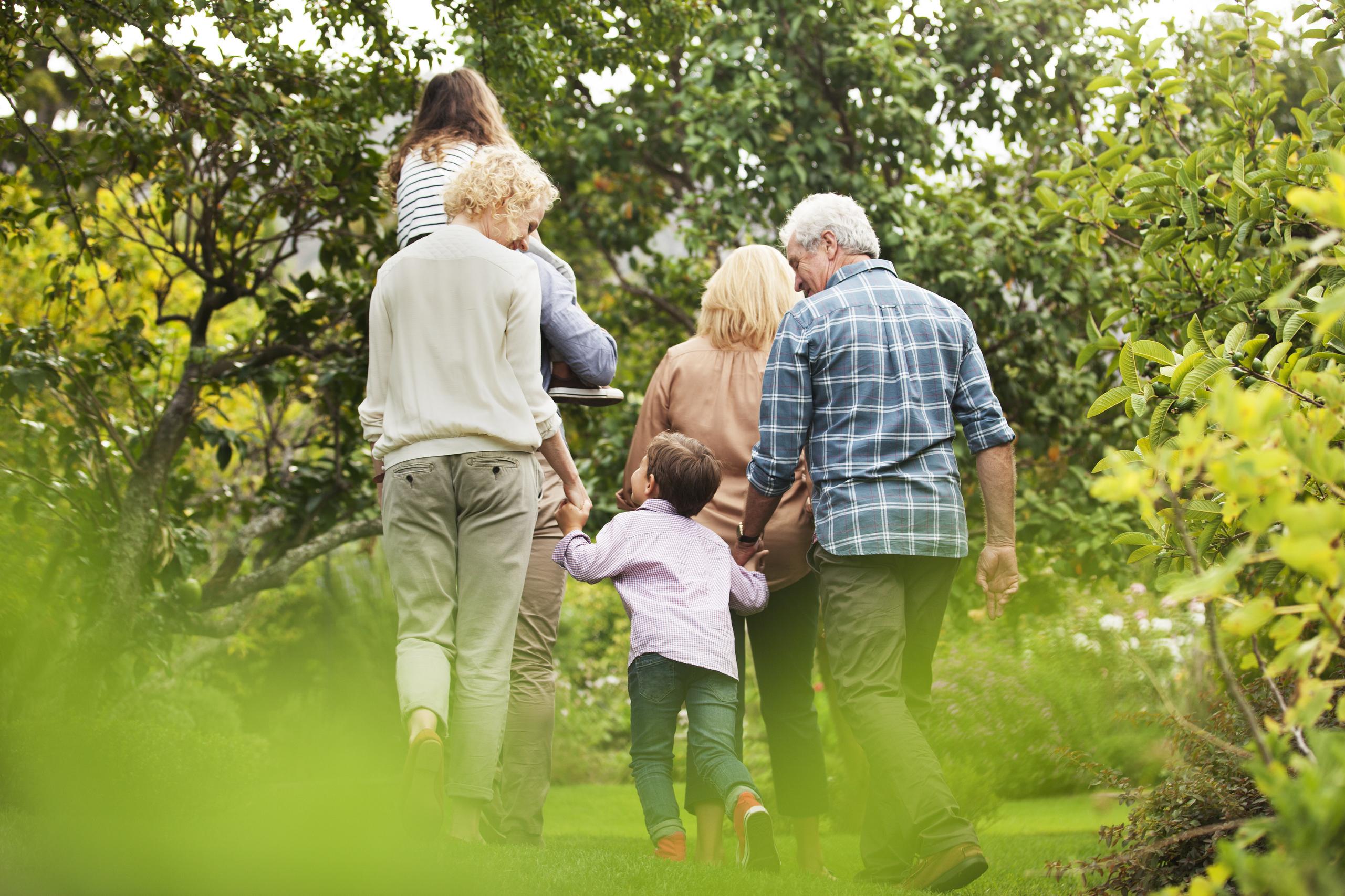 Multi-generational family walking together in garden with lush green trees