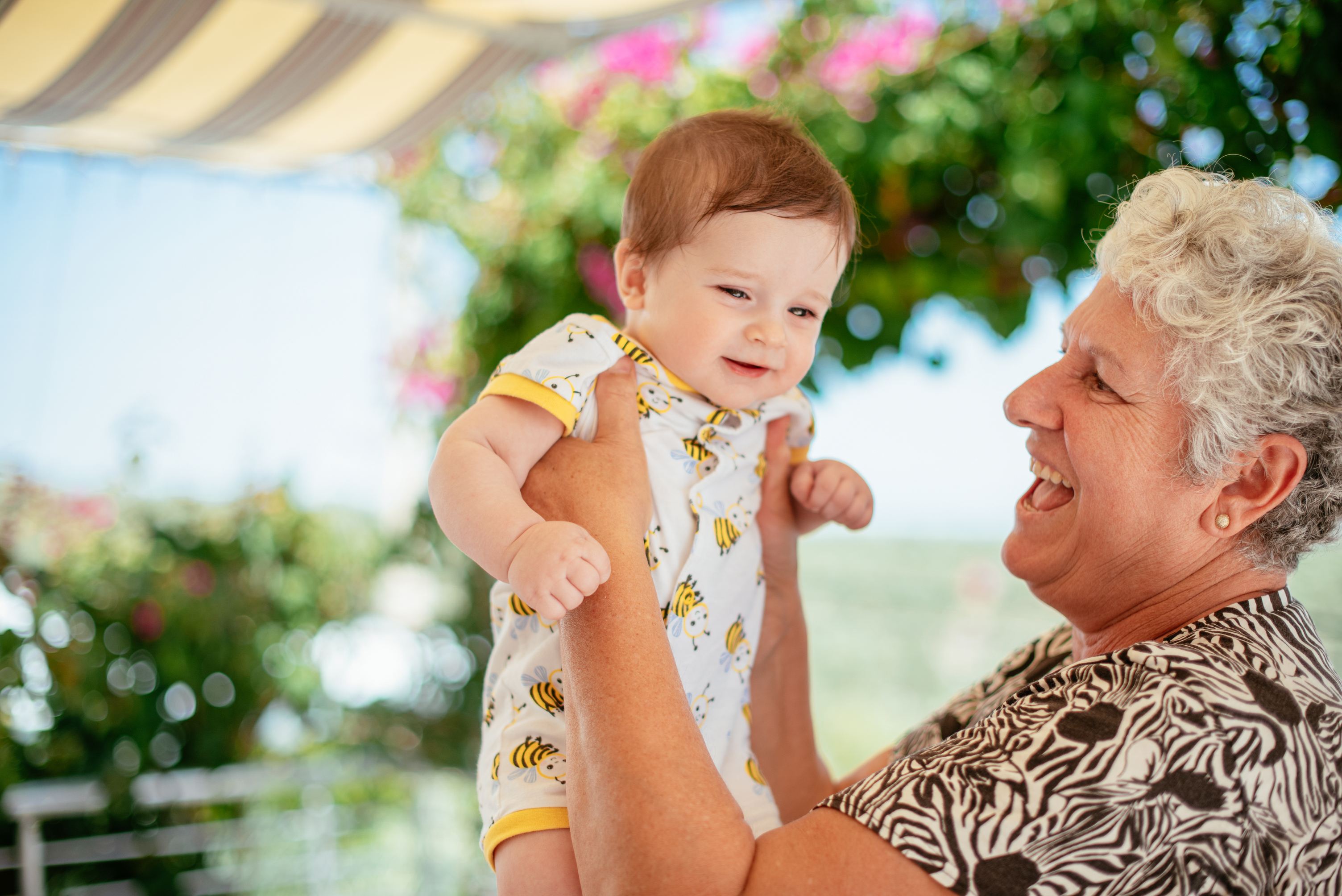 Smiling grandmother holding baby in bee-patterned outfit outdoors