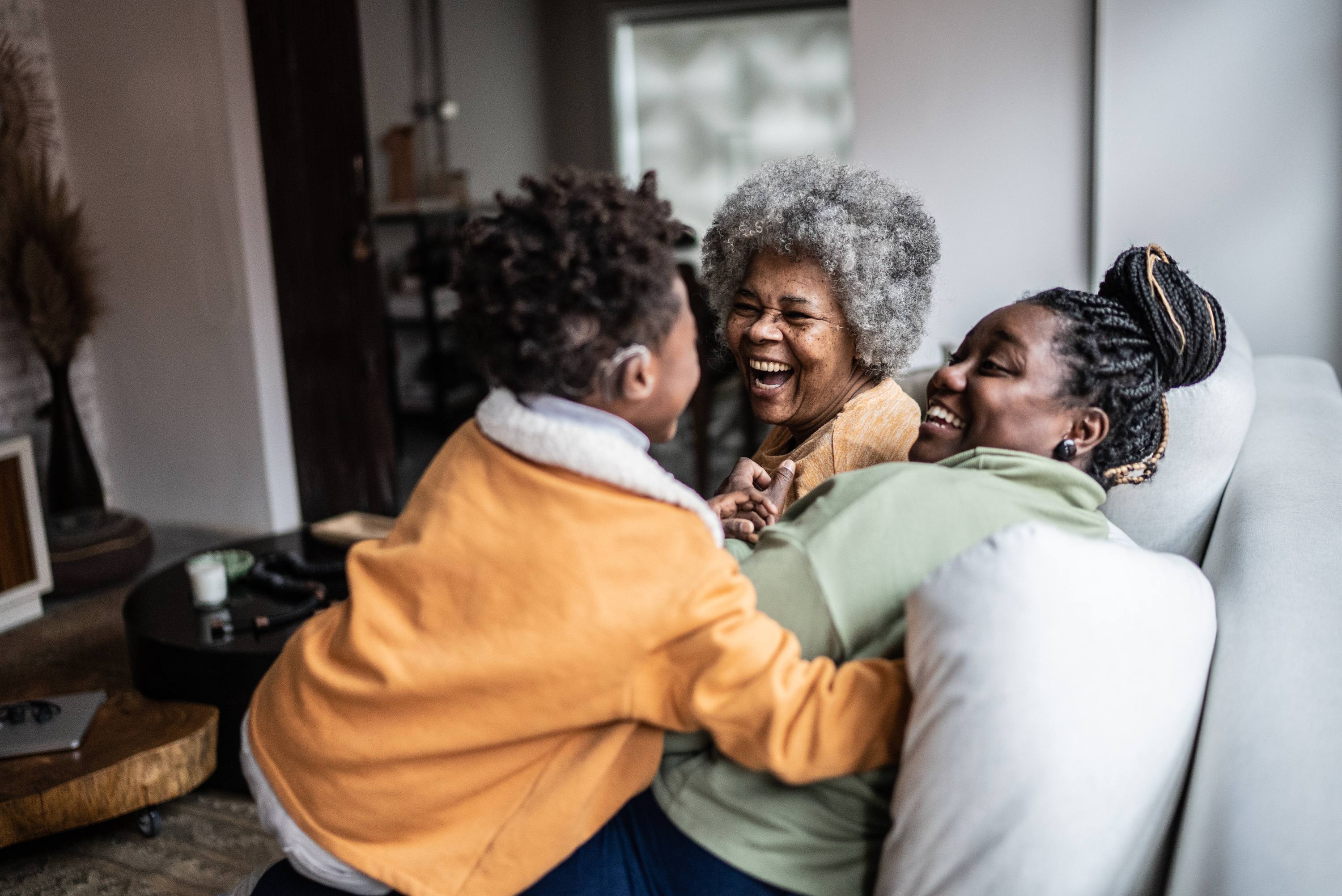 Three generations of Black family laughing and embracing together at home