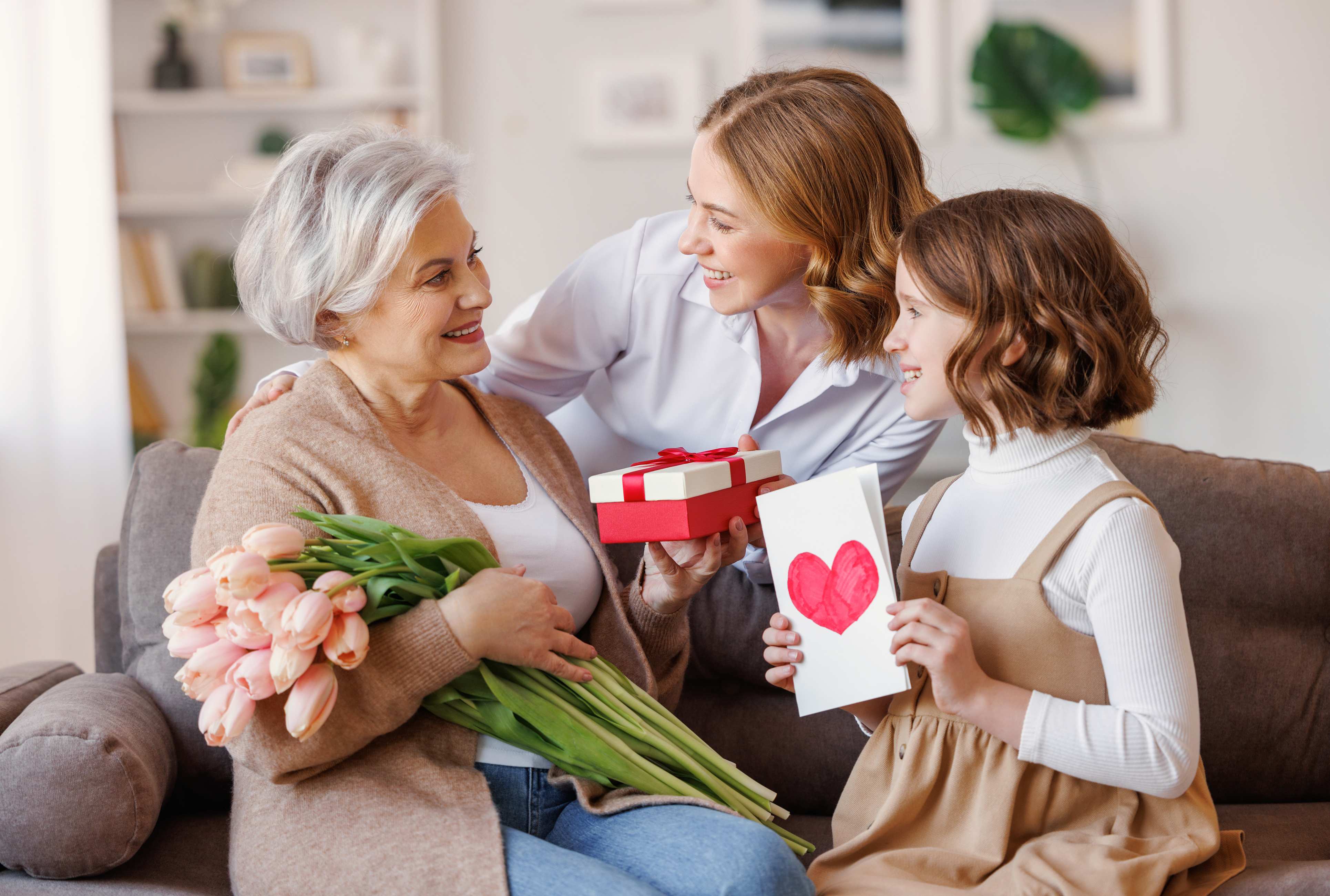 Three generations of women exchanging gifts and flowers on a couch