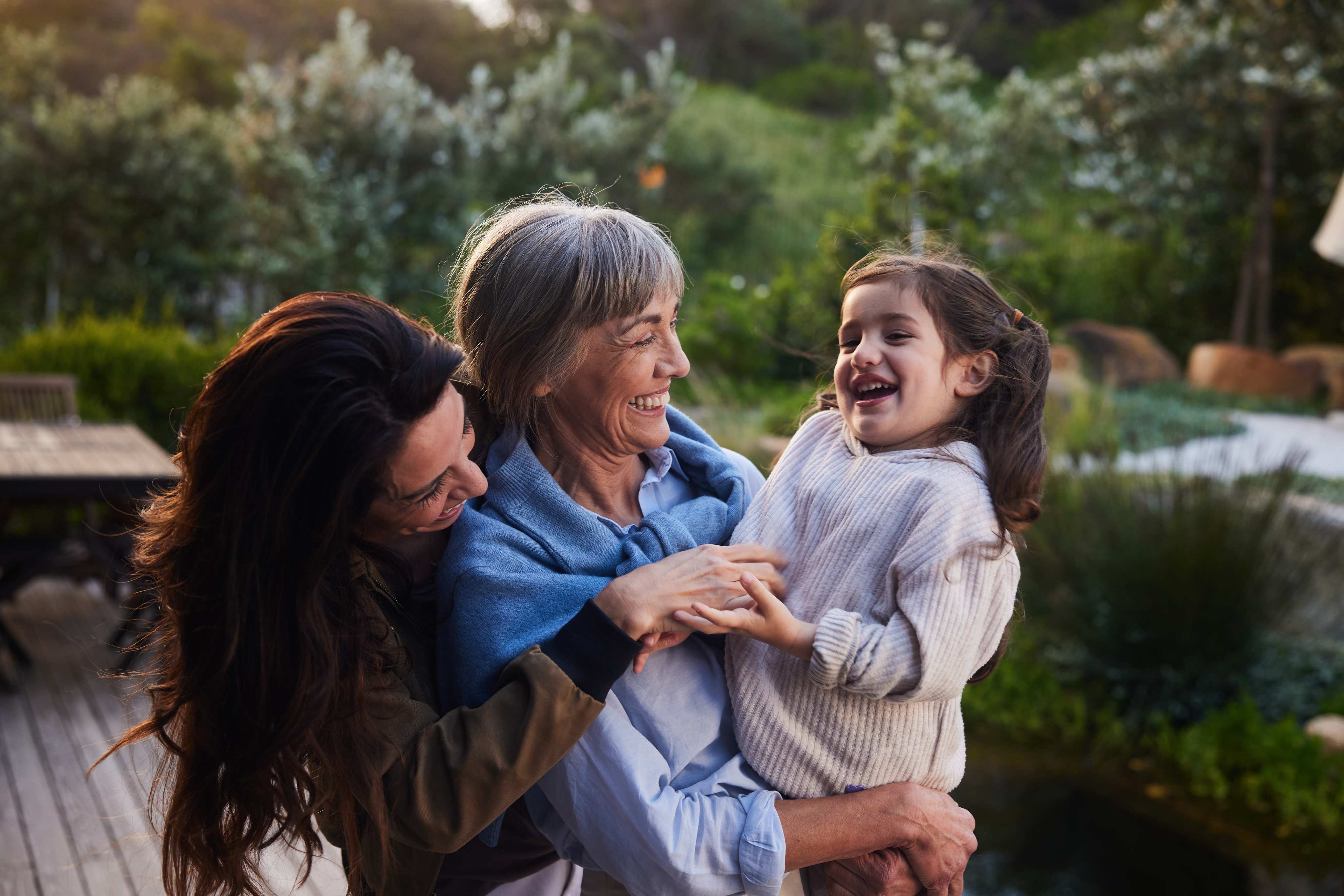 Three generations of women laughing together outdoors in garden setting