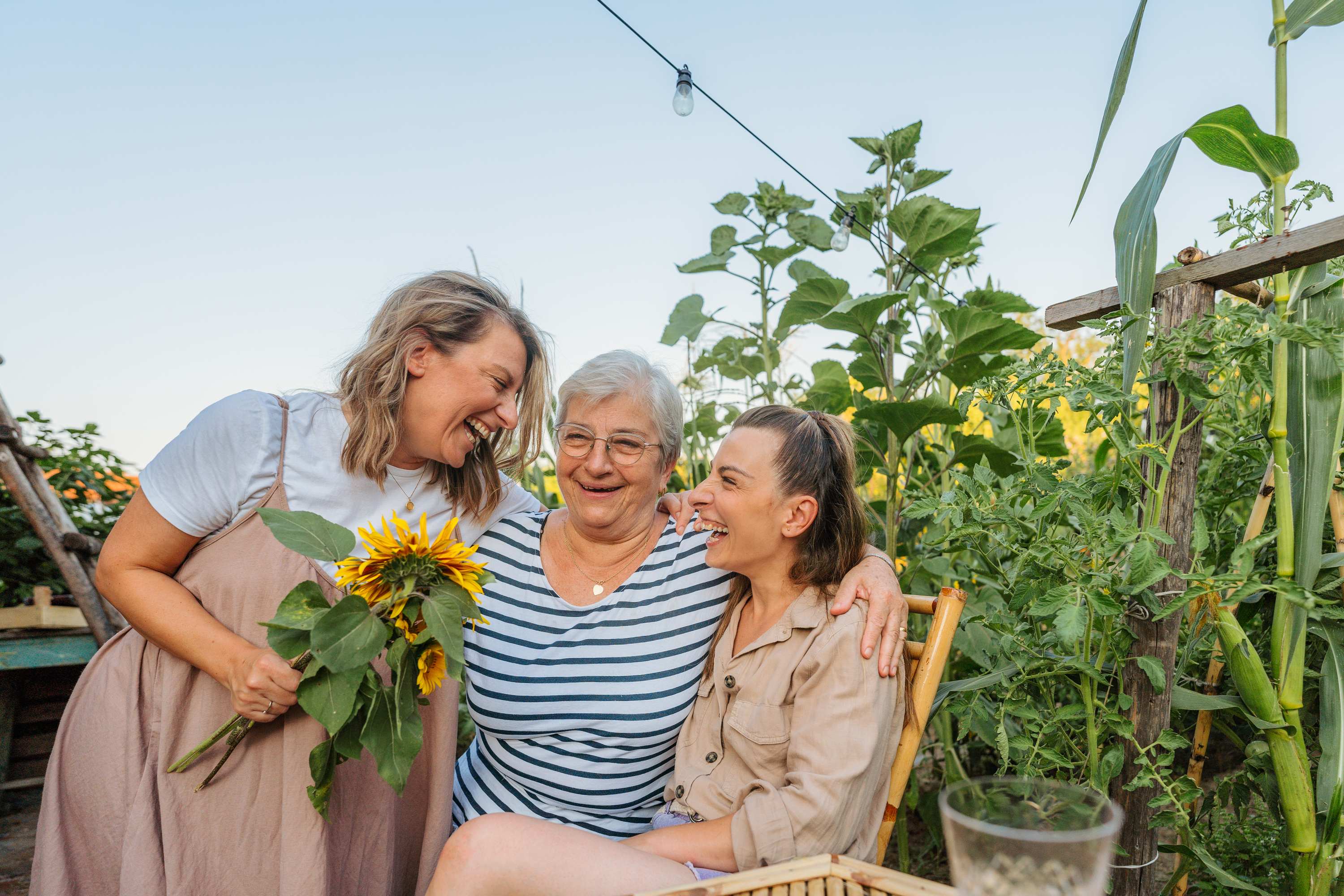 Three generations of women smiling together in a garden with sunflowers