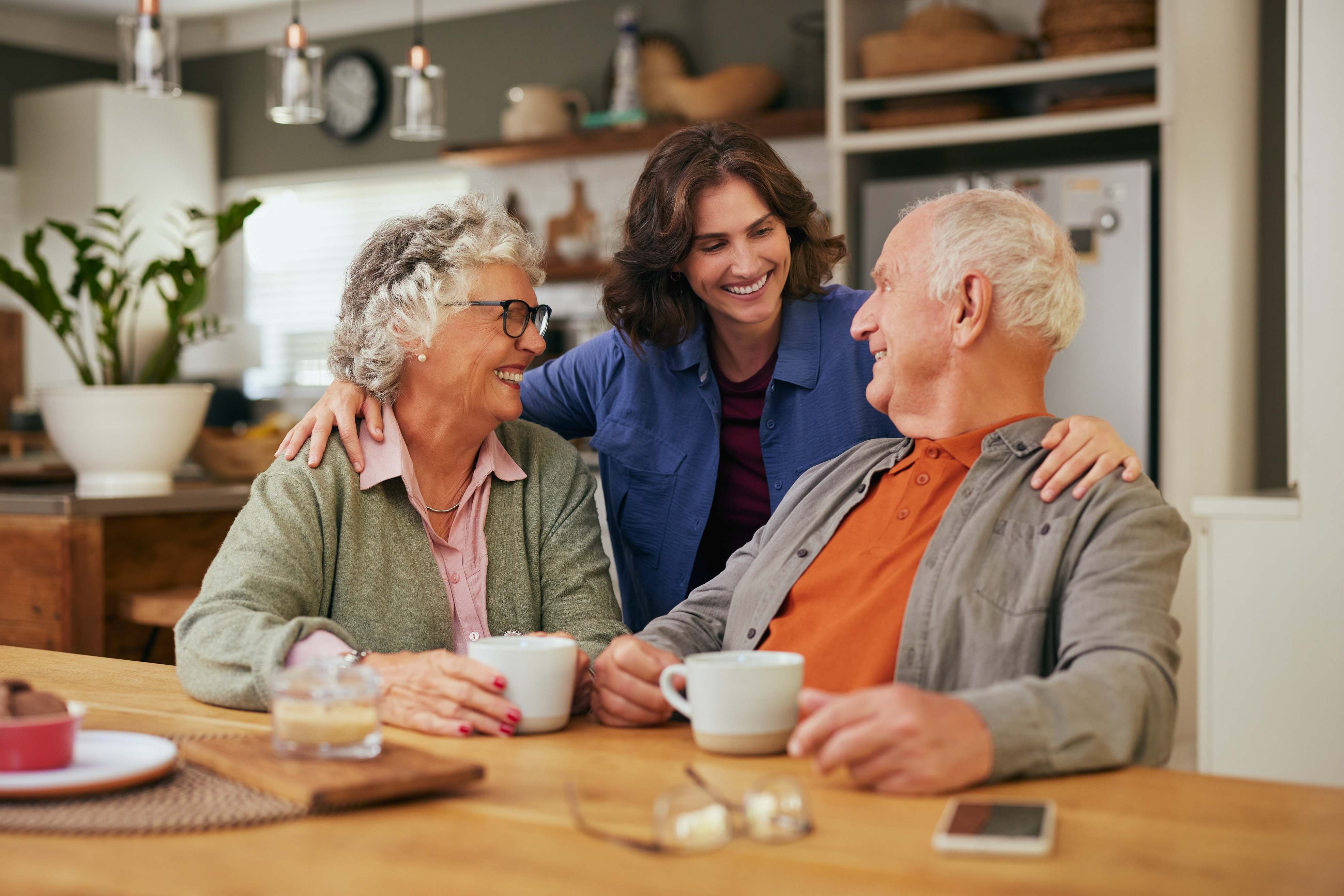 Three people smiling and enjoying coffee together in modern kitchen