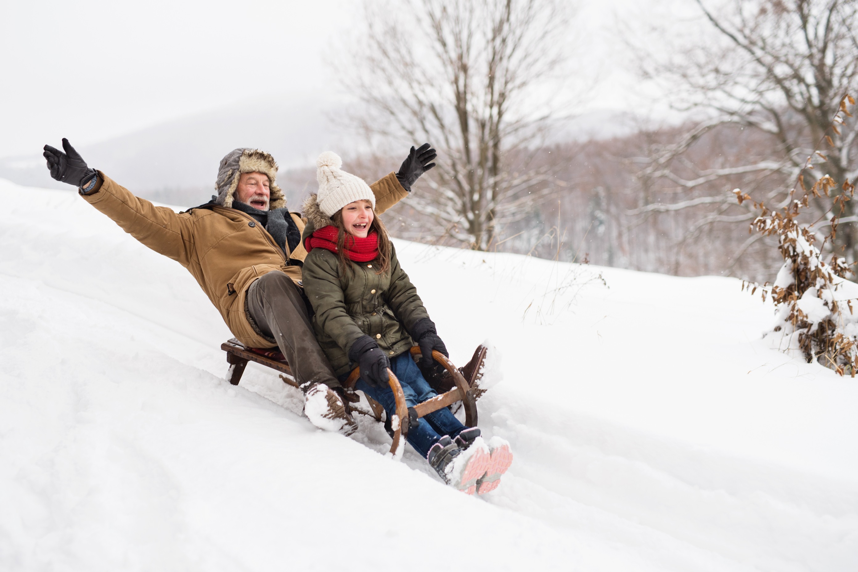 Two people sledding down snowy hill together laughing with winter clothing