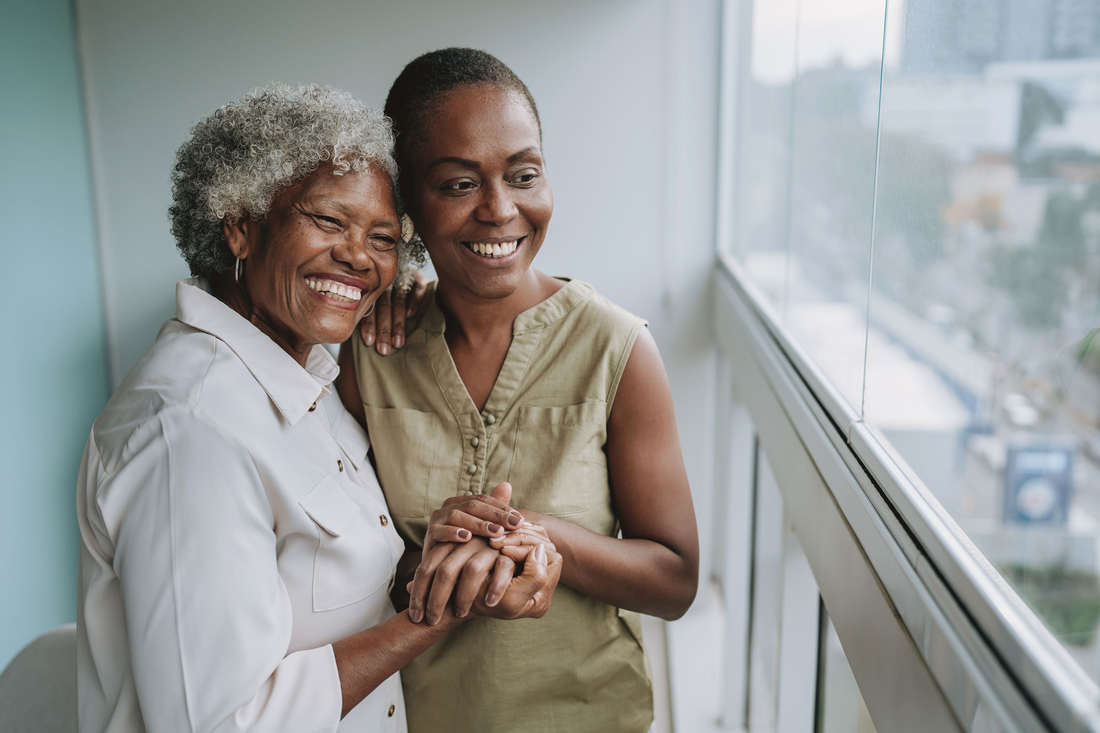 Two smiling Black women embracing near window, mother and daughter together