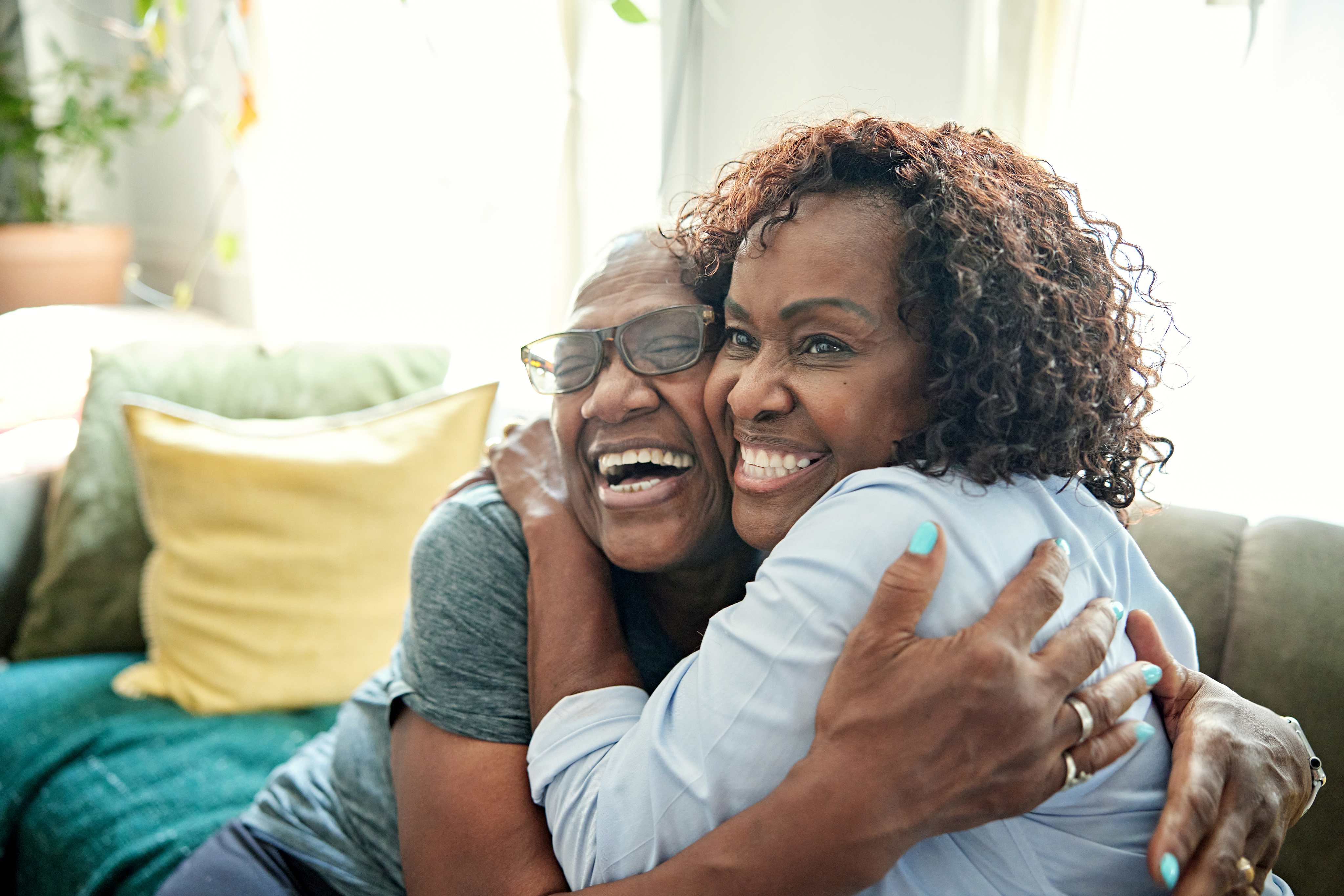 Two smiling women embracing warmly on a couch at home