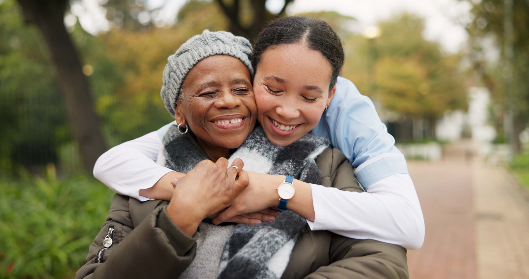 Two women embracing outdoors, younger woman hugging older woman from behind