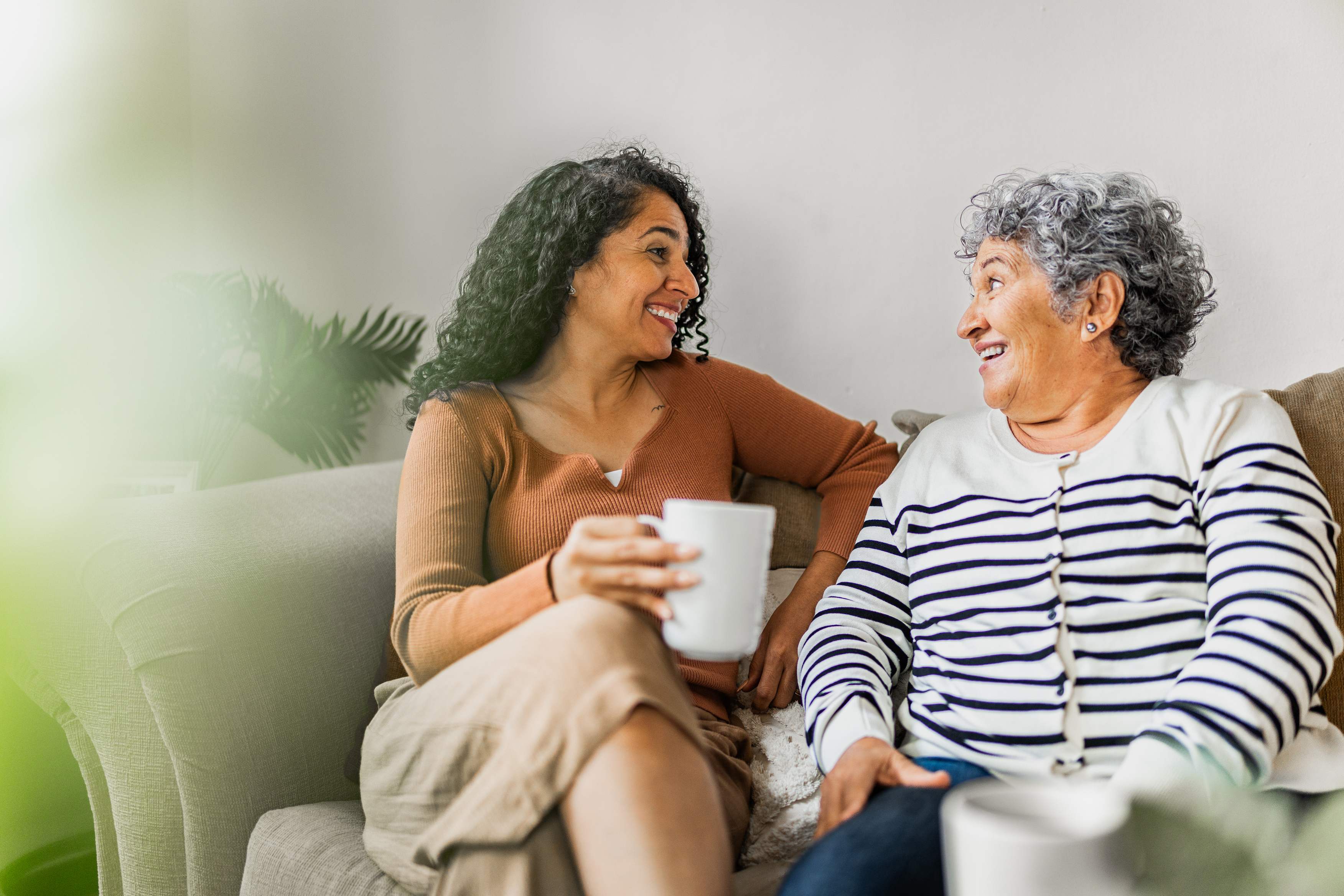 Two women having coffee and conversation on a couch smiling warmly