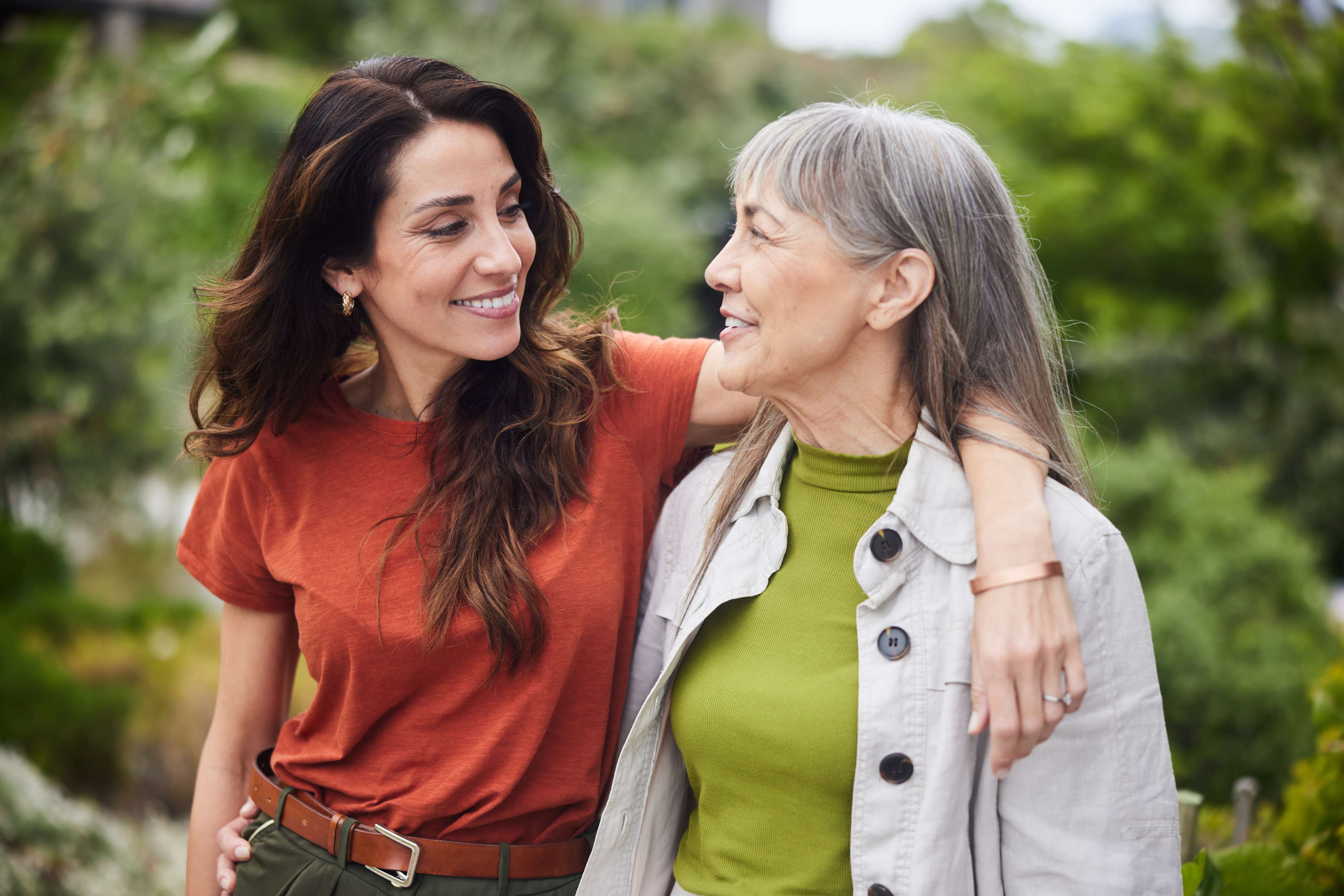 Two women smiling together outdoors with greenery in background