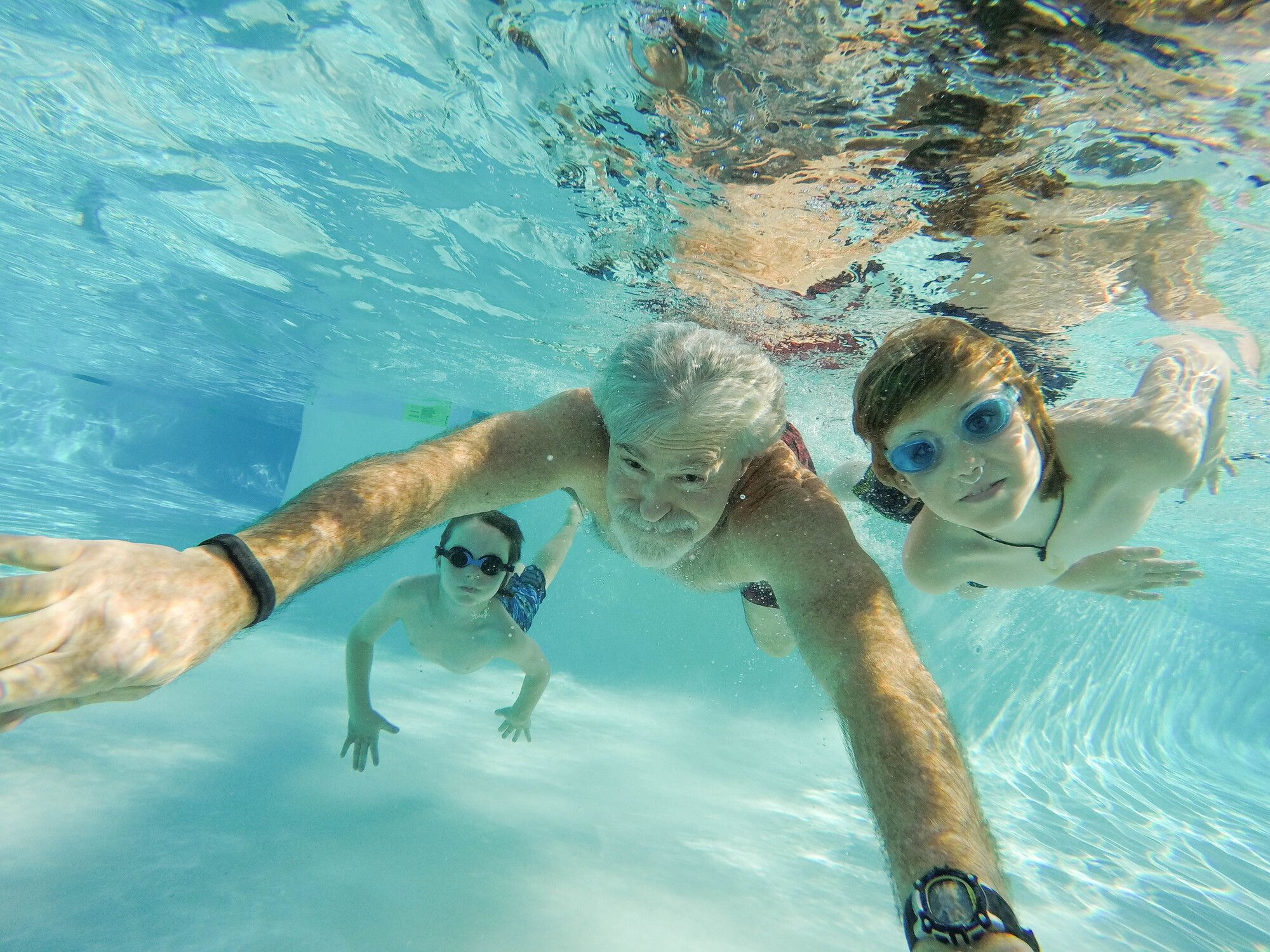 Underwater selfie of three people swimming in clear blue pool water