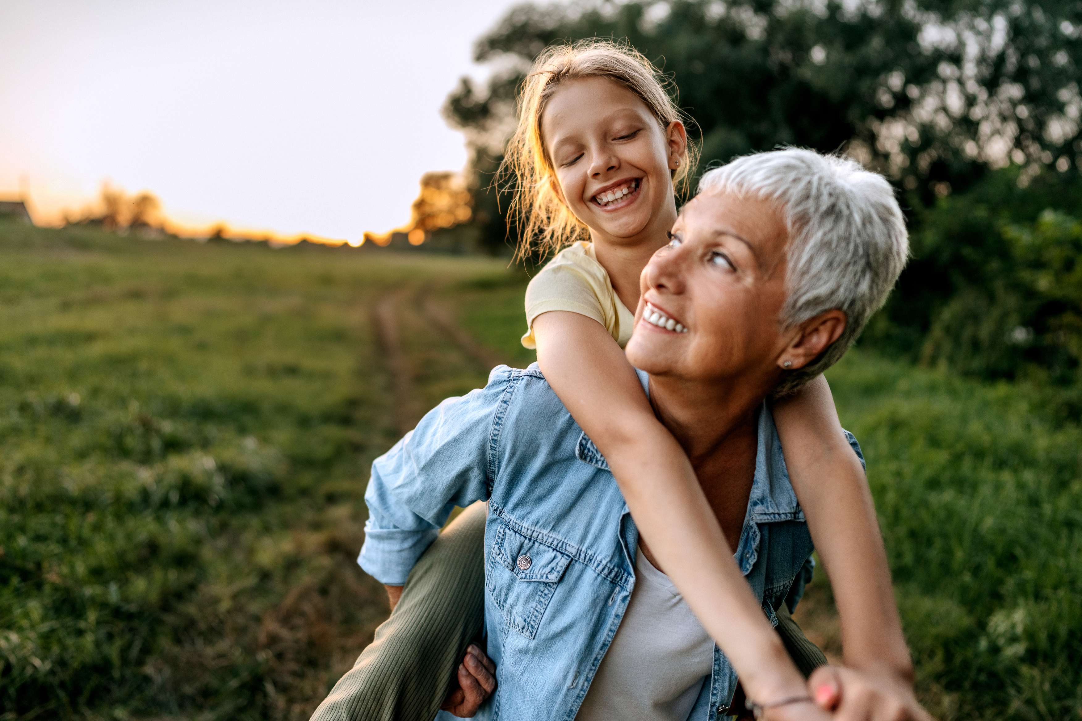 Young girl riding piggyback on grandmother outdoors at sunset