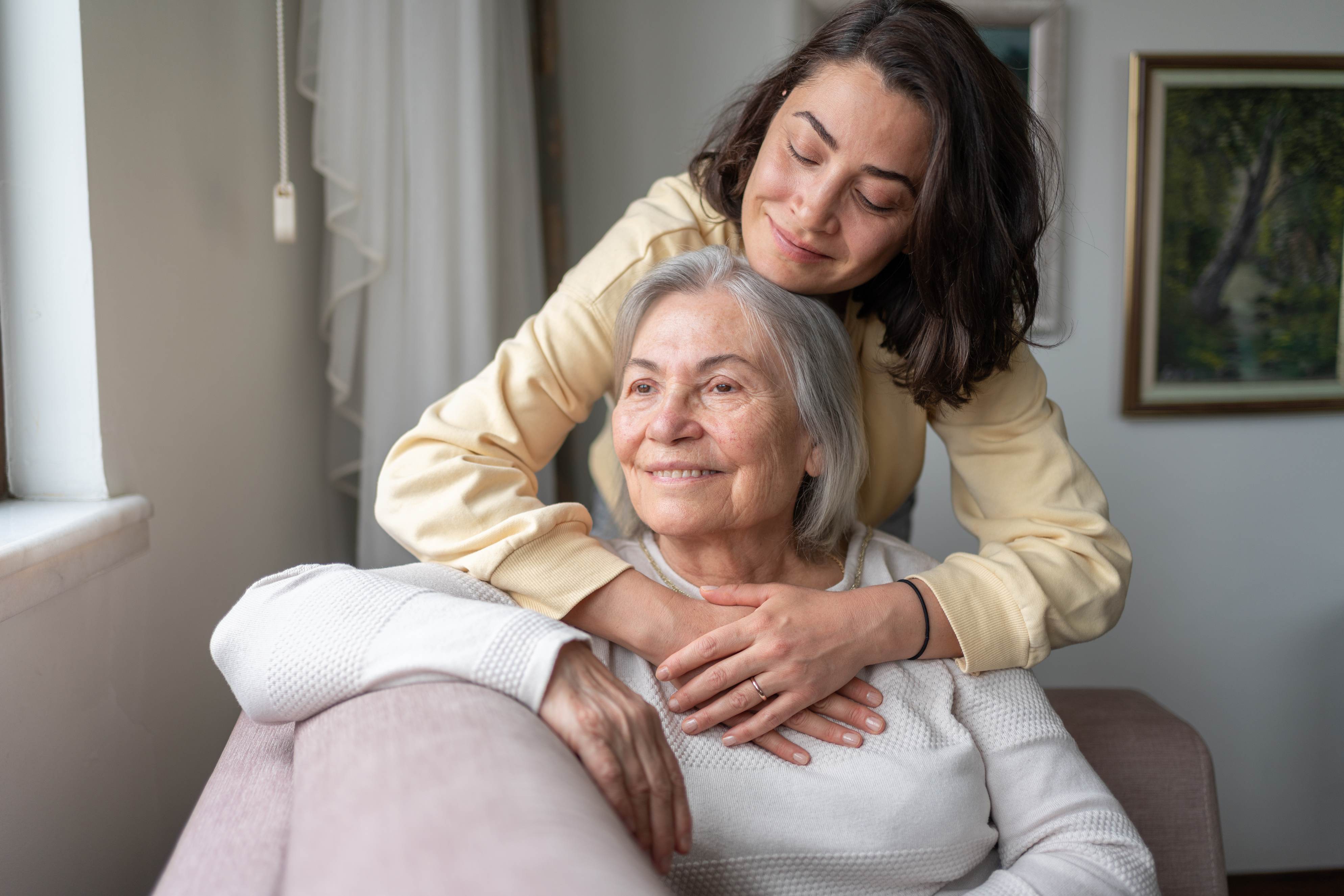 Young woman embracing elderly woman from behind in warm home setting