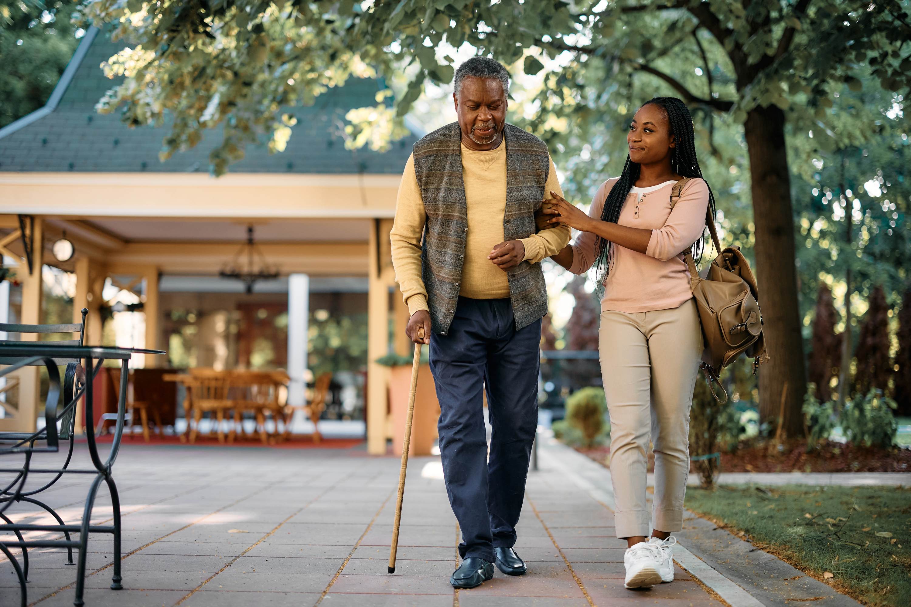 Young woman helping elderly man with cane walk in park