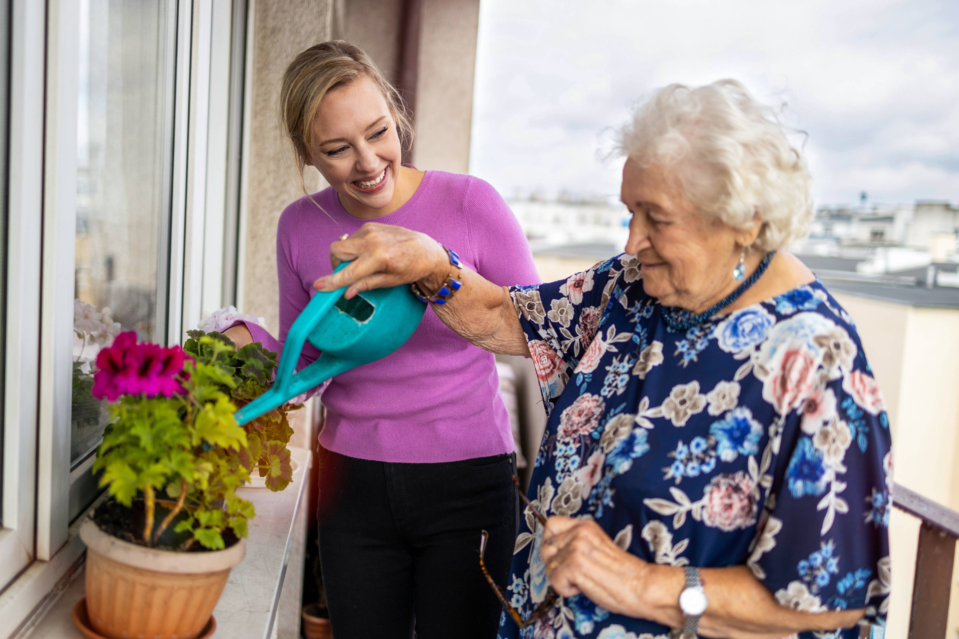 Young woman helping elderly woman water plants by window