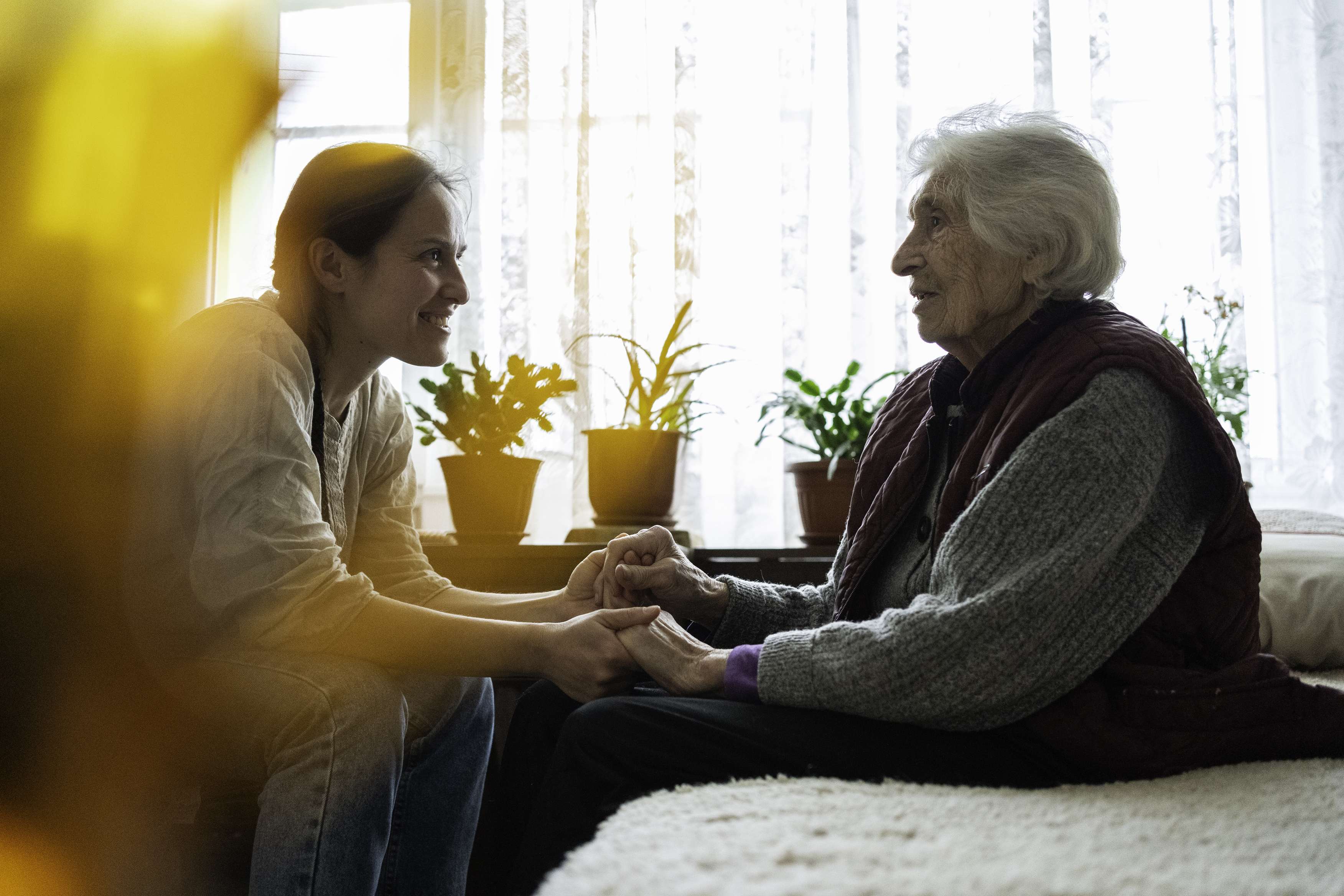 Young woman holding hands with elderly woman in sunlit room